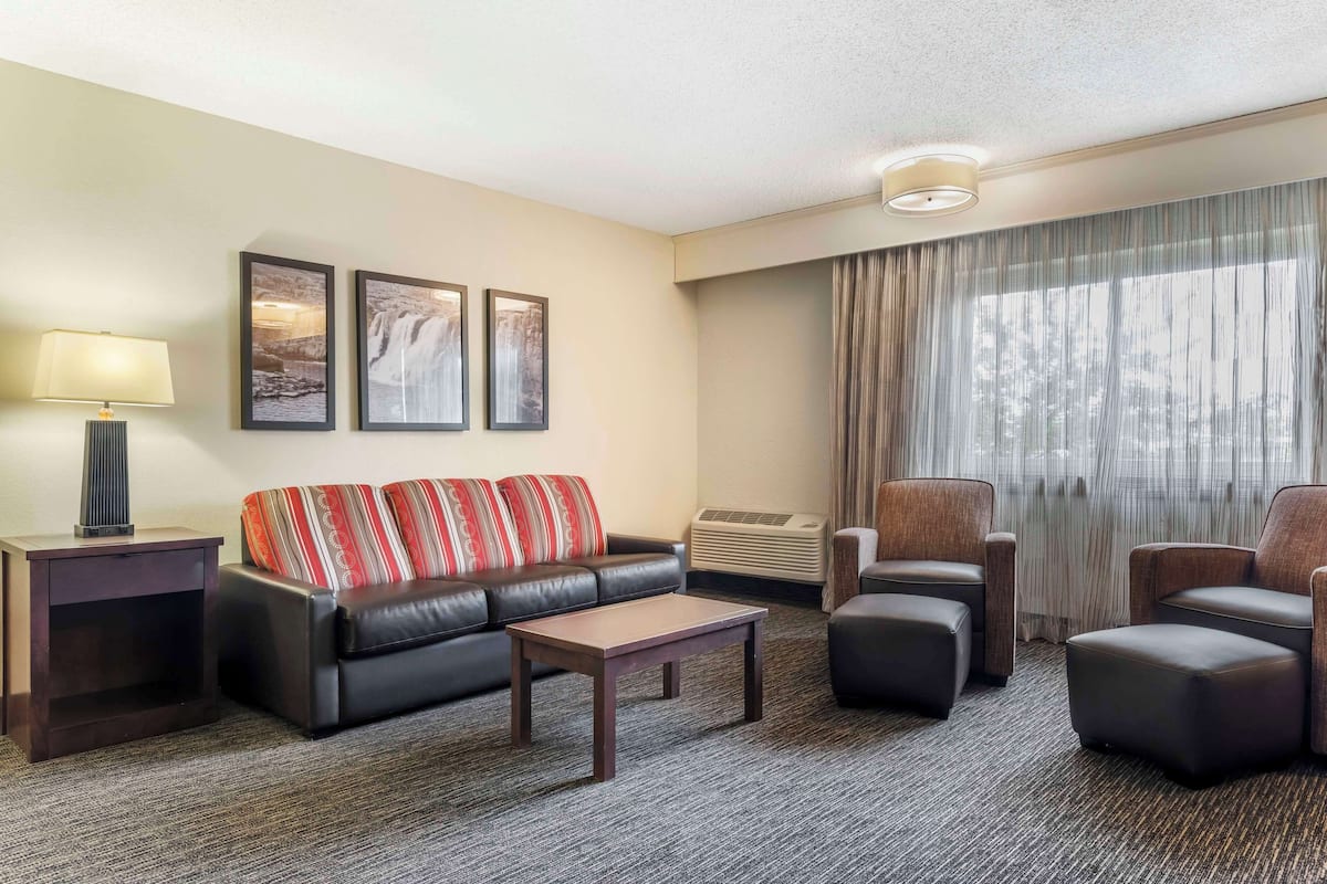 Ein Hotelzimmer mit einer Couch, zwei Sesseln, einem Couchtisch, einer Lampe und zwei gerahmten Bildern an der Wand.