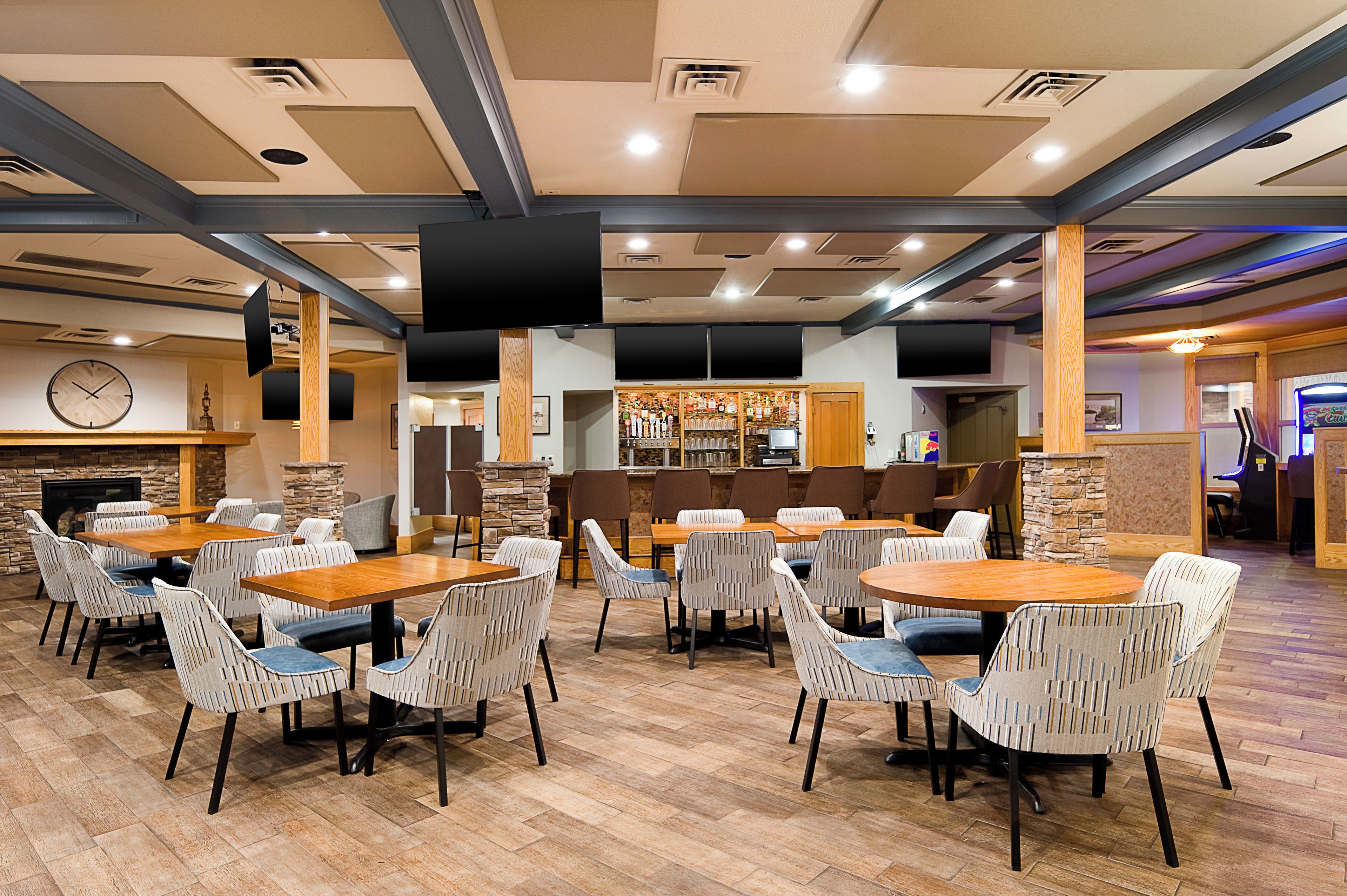 A spacious indoor dining area with multiple tables and chairs, a bar area with a variety of bottles, and a clock on the wall.