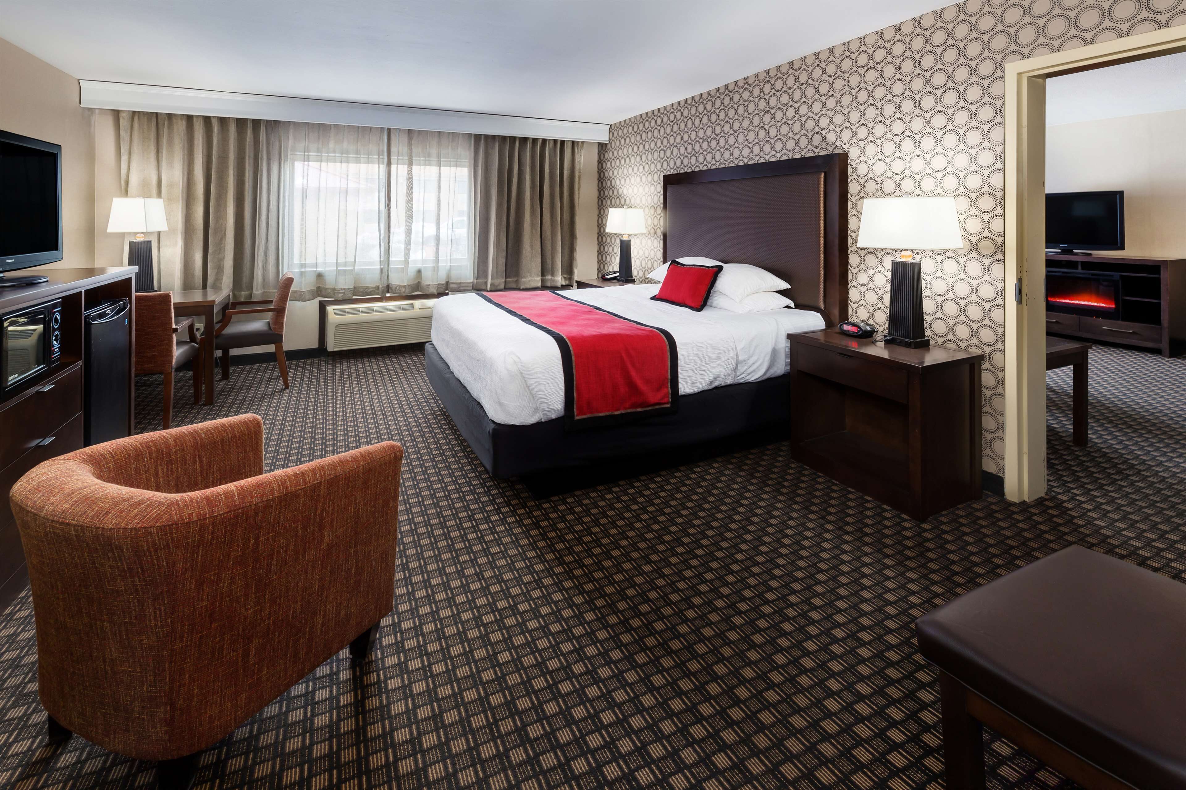 A hotel room with a bed, a desk, a chair, a television, and a fireplace.