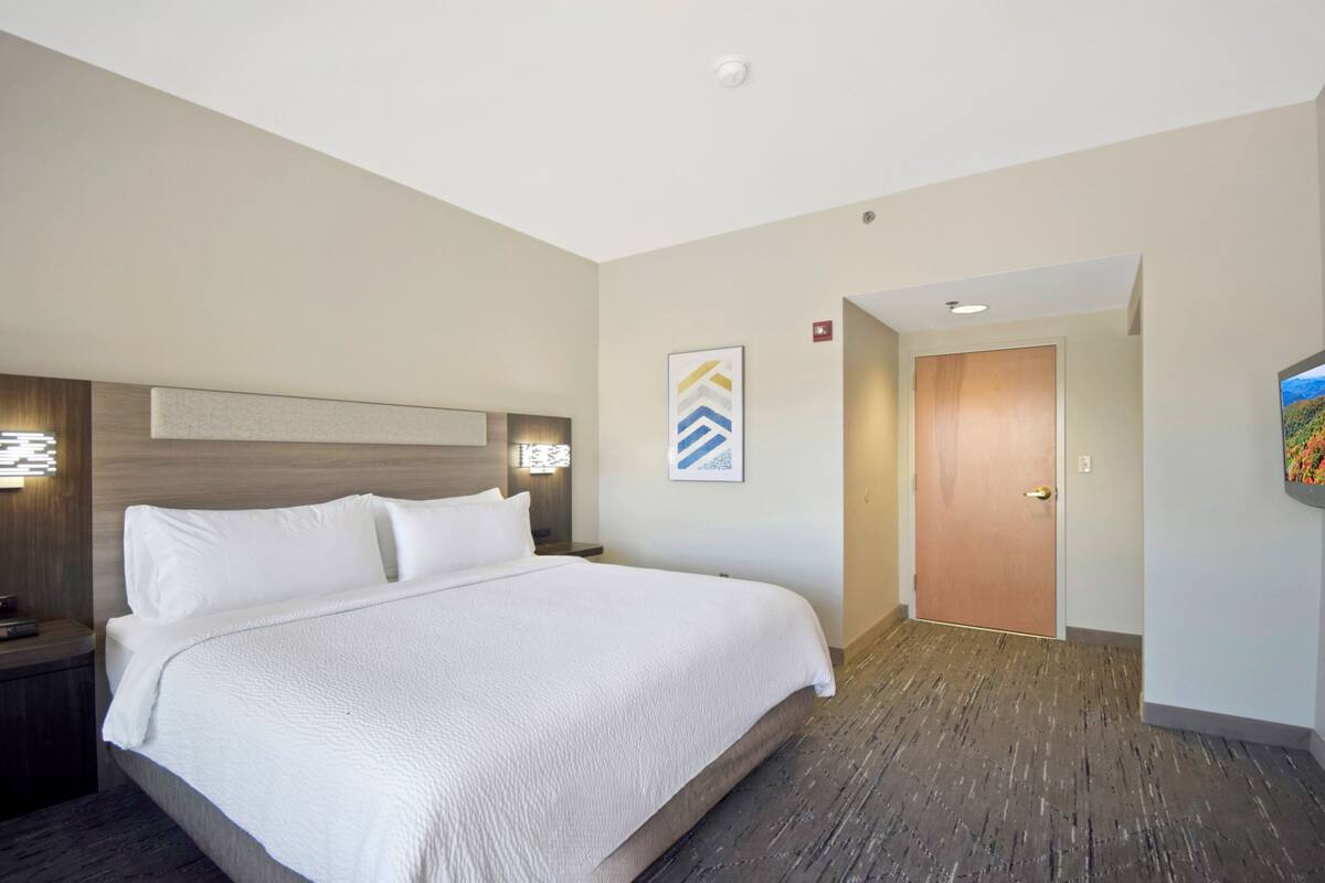 A hotel room with a large bed, a nightstand, a wall-mounted light, and a door.