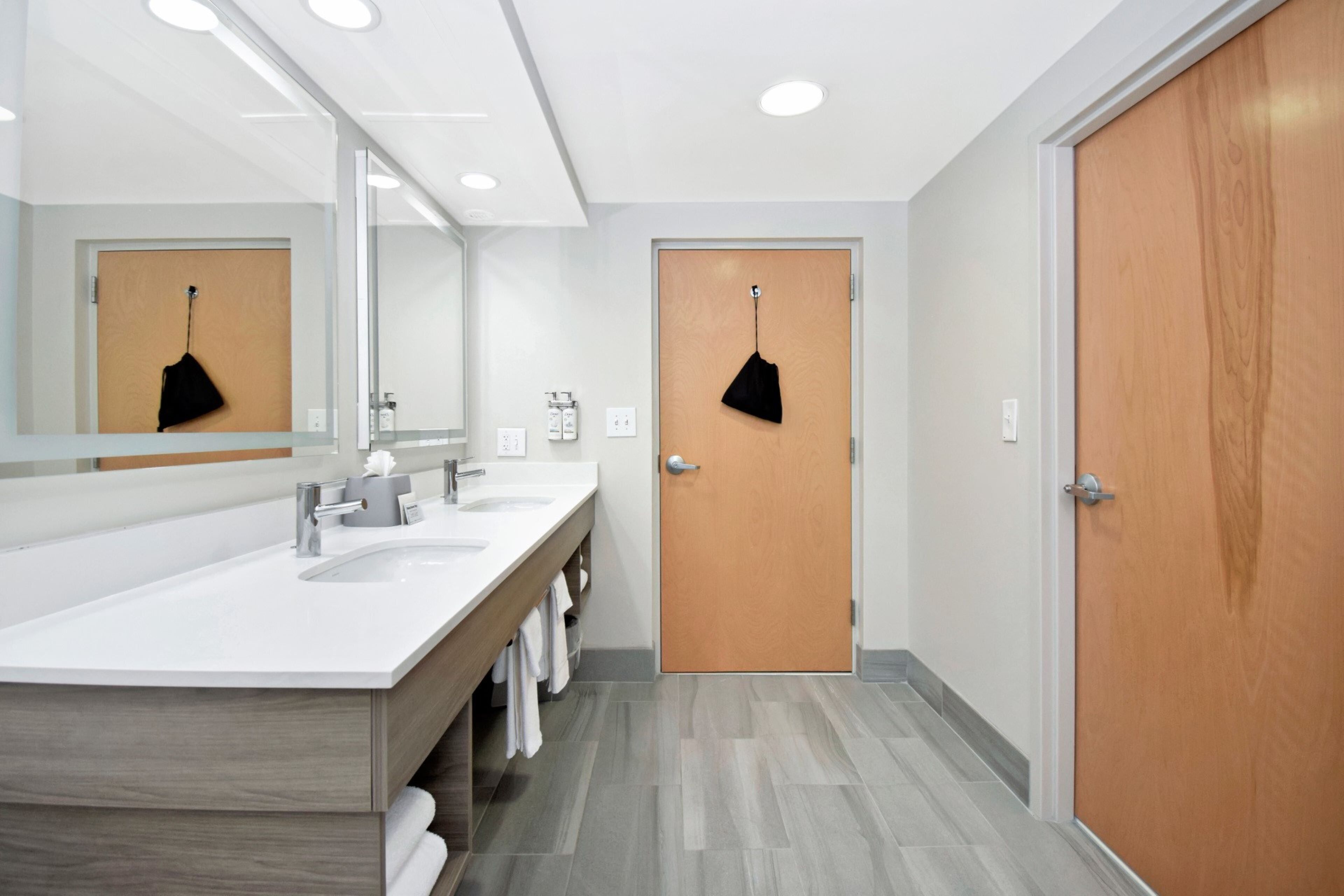 Un baño moderno con un espejo grande, dos lavamanos y una puerta de madera.
