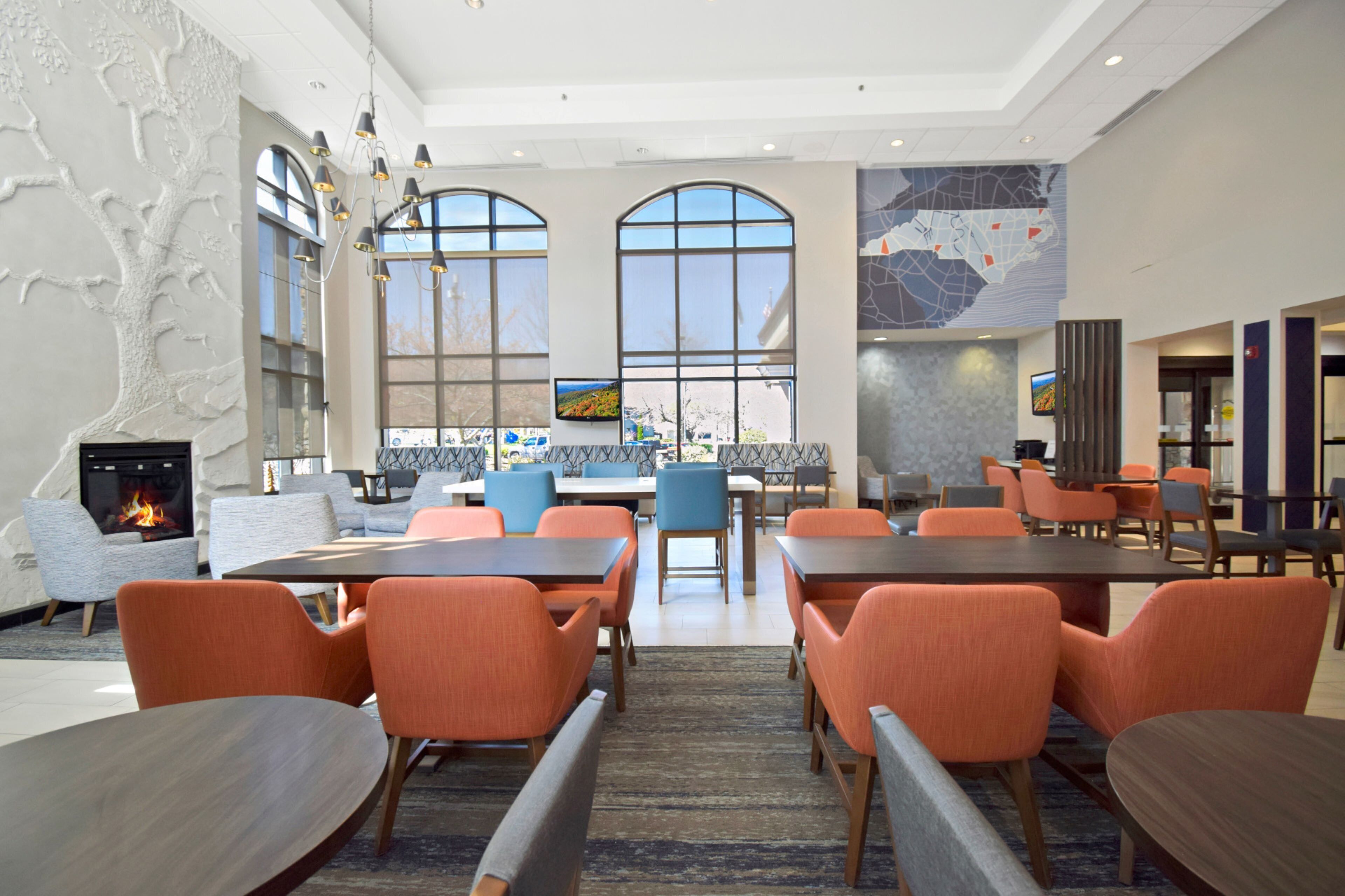 A modern hotel lobby with a fireplace, large windows, and a map on the wall.