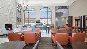 A modern hotel lobby with a fireplace, large windows, and a map on the wall.