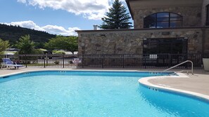 A swimming pool with a lifeguard warning sign, a stone building with a large window, and a mountain in the background.