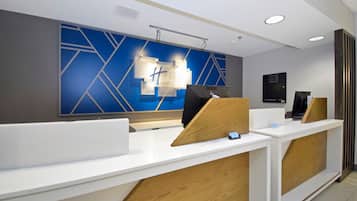 A modern reception desk with a blue geometric wall design, a white countertop, and wooden accents.
