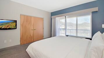 A hotel room with a large bed, a television on the wall, a wooden door, and a window with a view.