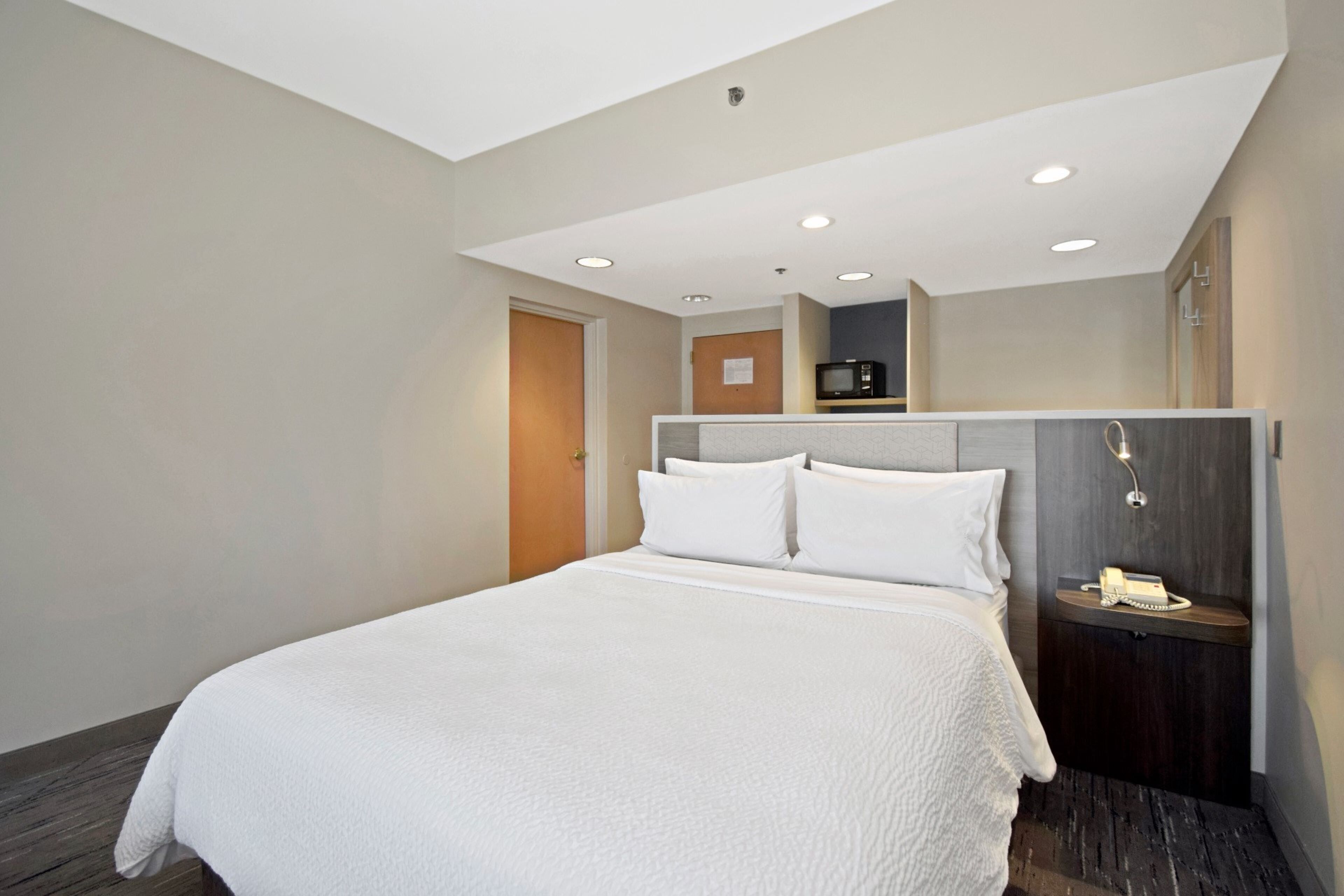 A hotel room with a large bed, a bedside table with a lamp, a microwave, and a telephone.