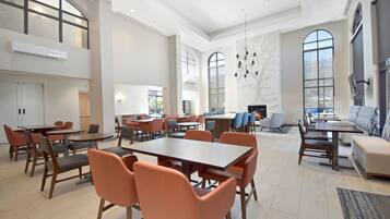 A spacious dining area with multiple tables and chairs, large windows, and a modern chandelier.