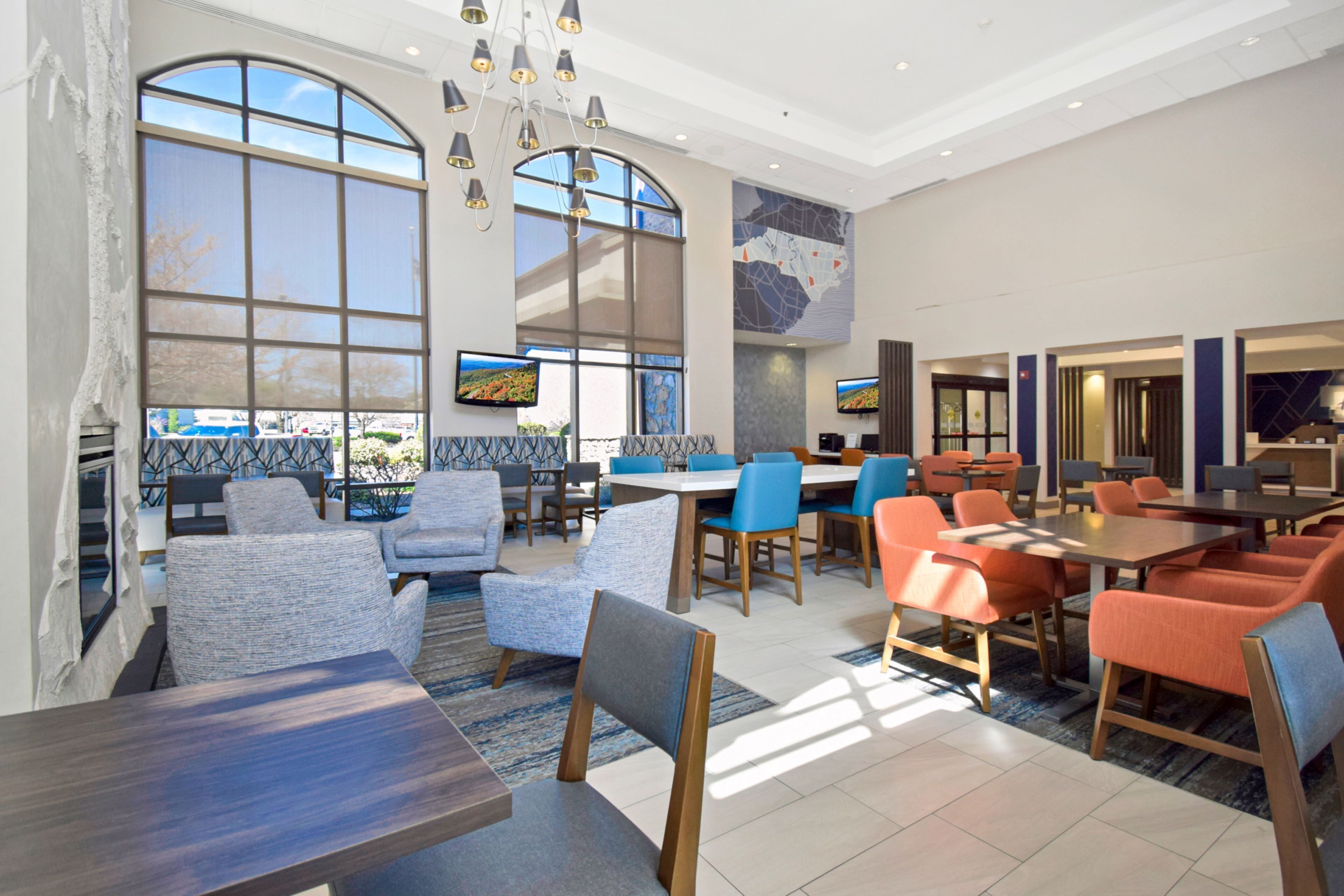 A modern hotel lobby with large windows, comfortable seating areas, and a central dining space.