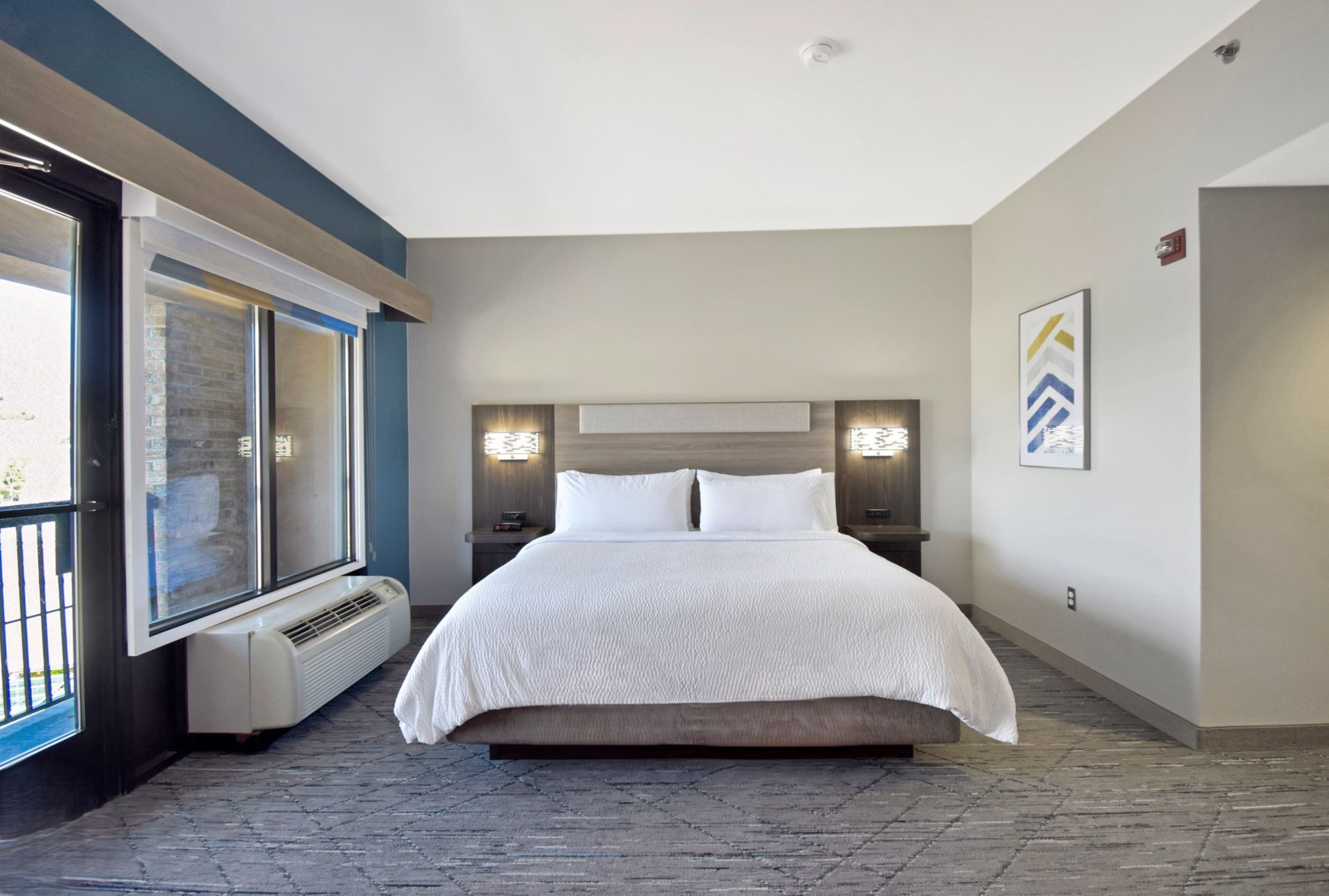 A modern hotel room with a large bed, a window with a view, a built-in heater, and two bedside lamps.