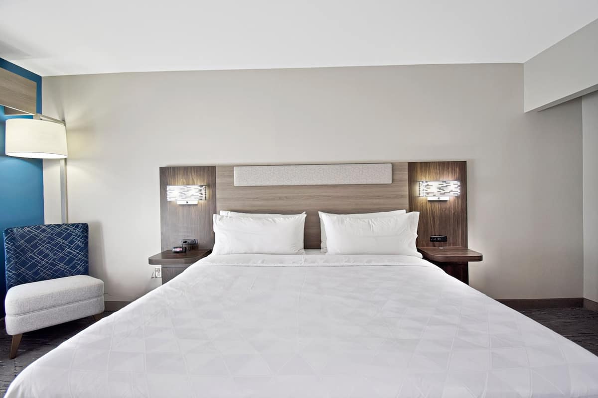 A hotel room with a large bed, two bedside tables, a nightstand, a lamp, and a chair.