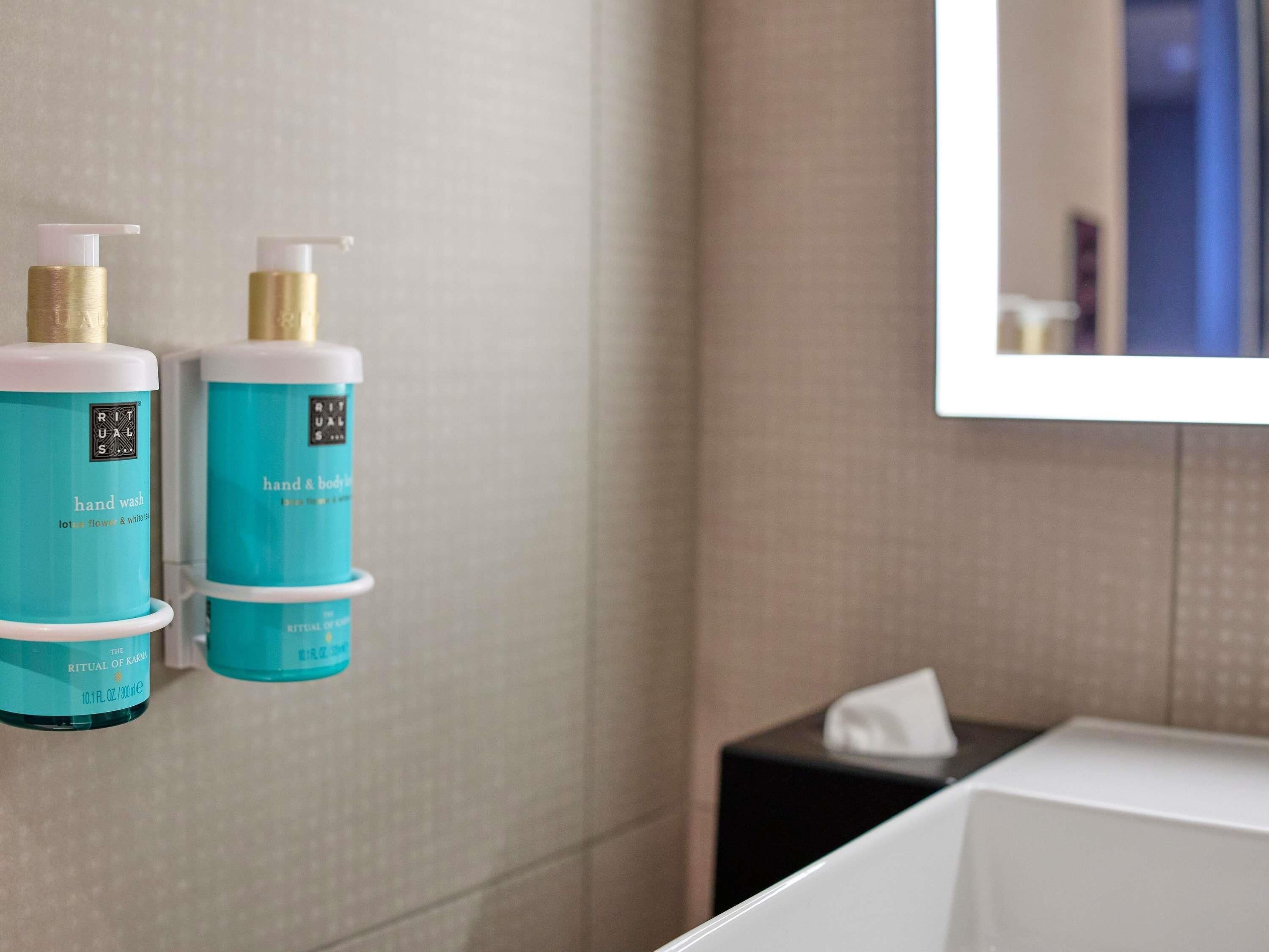 Un bagno con due flaconi di sapone per le mani color acquamarina, un lavandino bianco e uno specchio.