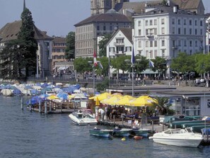 Ein Yachthafen mit vertäuten Booten, eine Uferpromenade und Gebäude mit Geschäften.