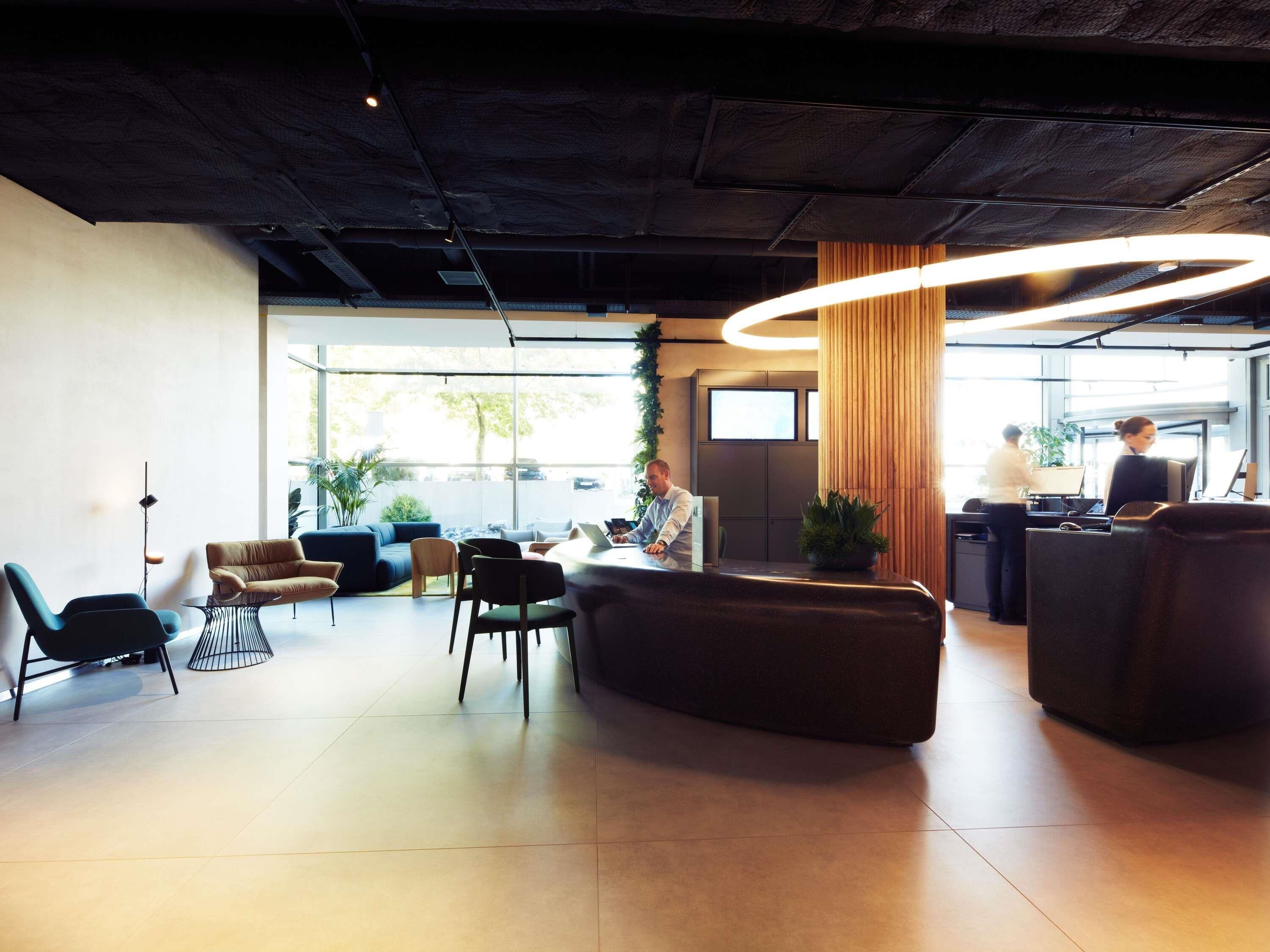 A modern lobby with a reception desk, seating area, and large windows.