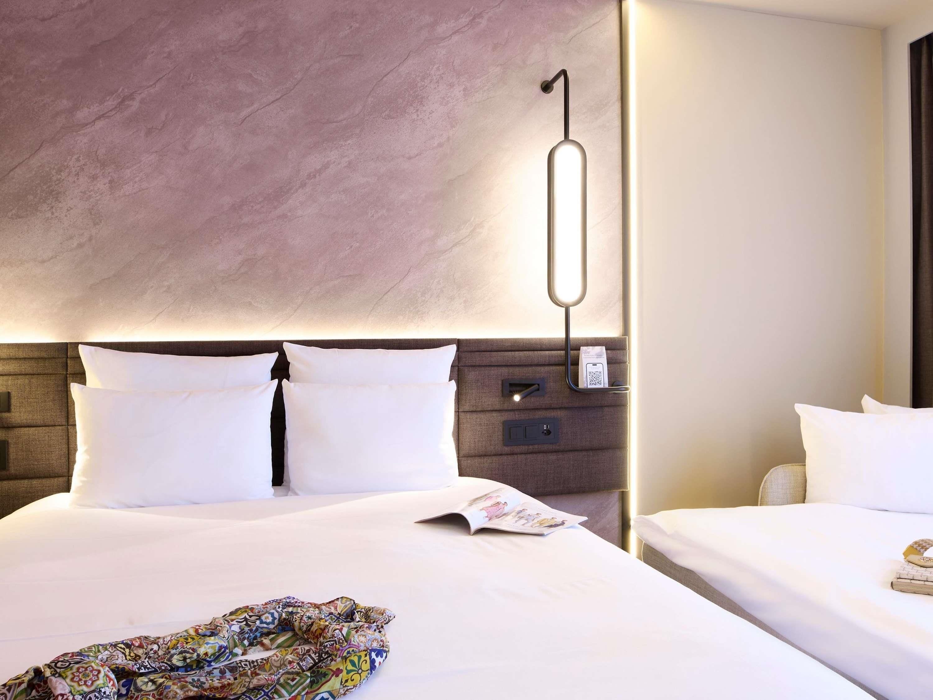 A hotel room with a large bed, a bedside table, a wall-mounted light, and a power outlet.