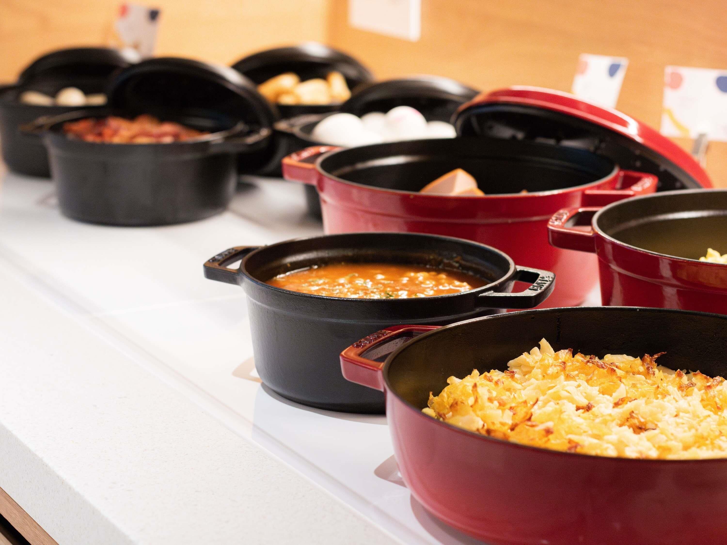 A buffet line with various dishes in black and red pots.