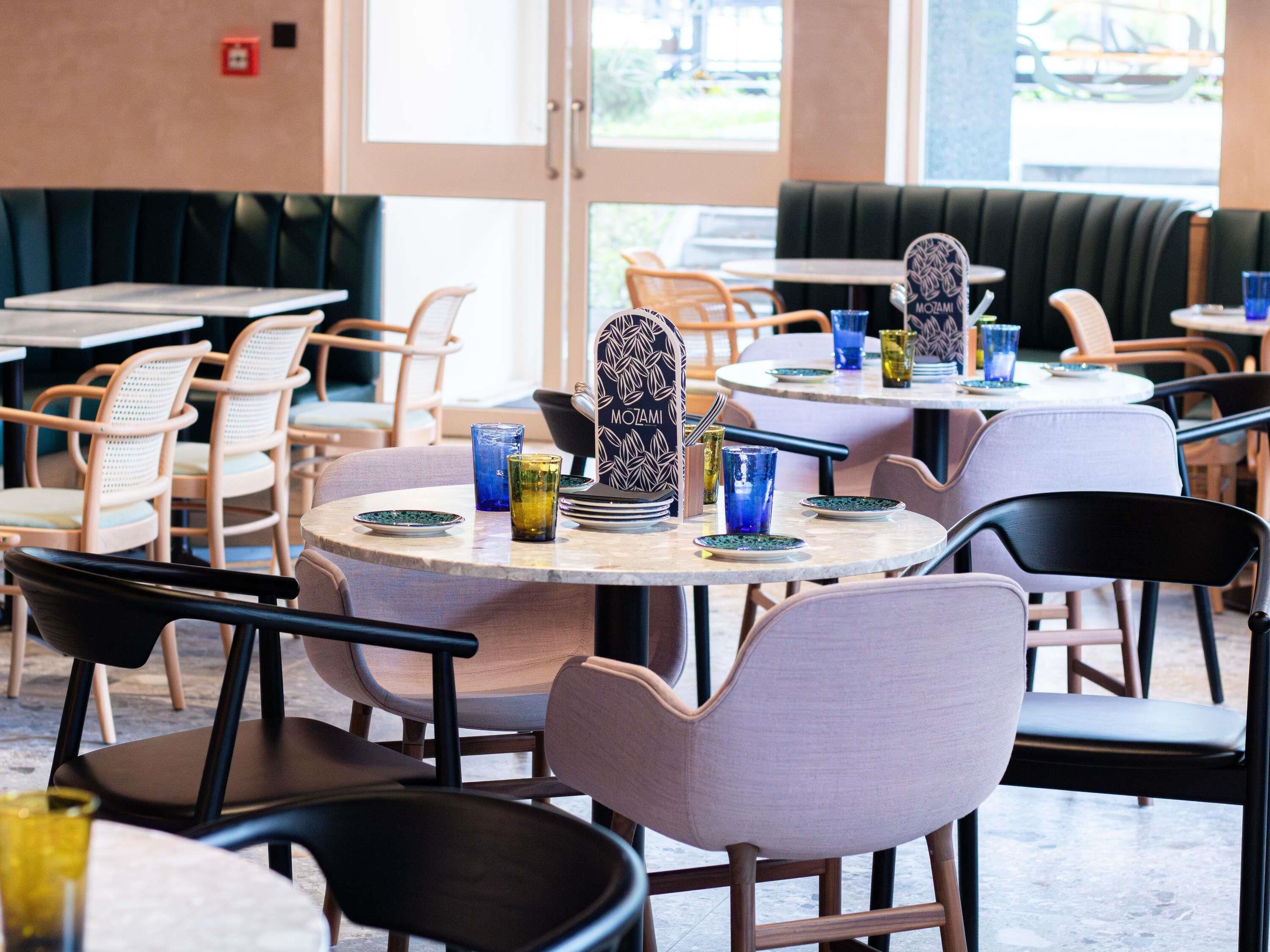 Un interno di ristorante con tavoli rotondi, sedie e una zona con banconi.