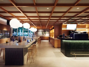 A modern bar area with a long counter, stools, and a television screen. - Novotel Zurich Airport Messe (Opfikon)