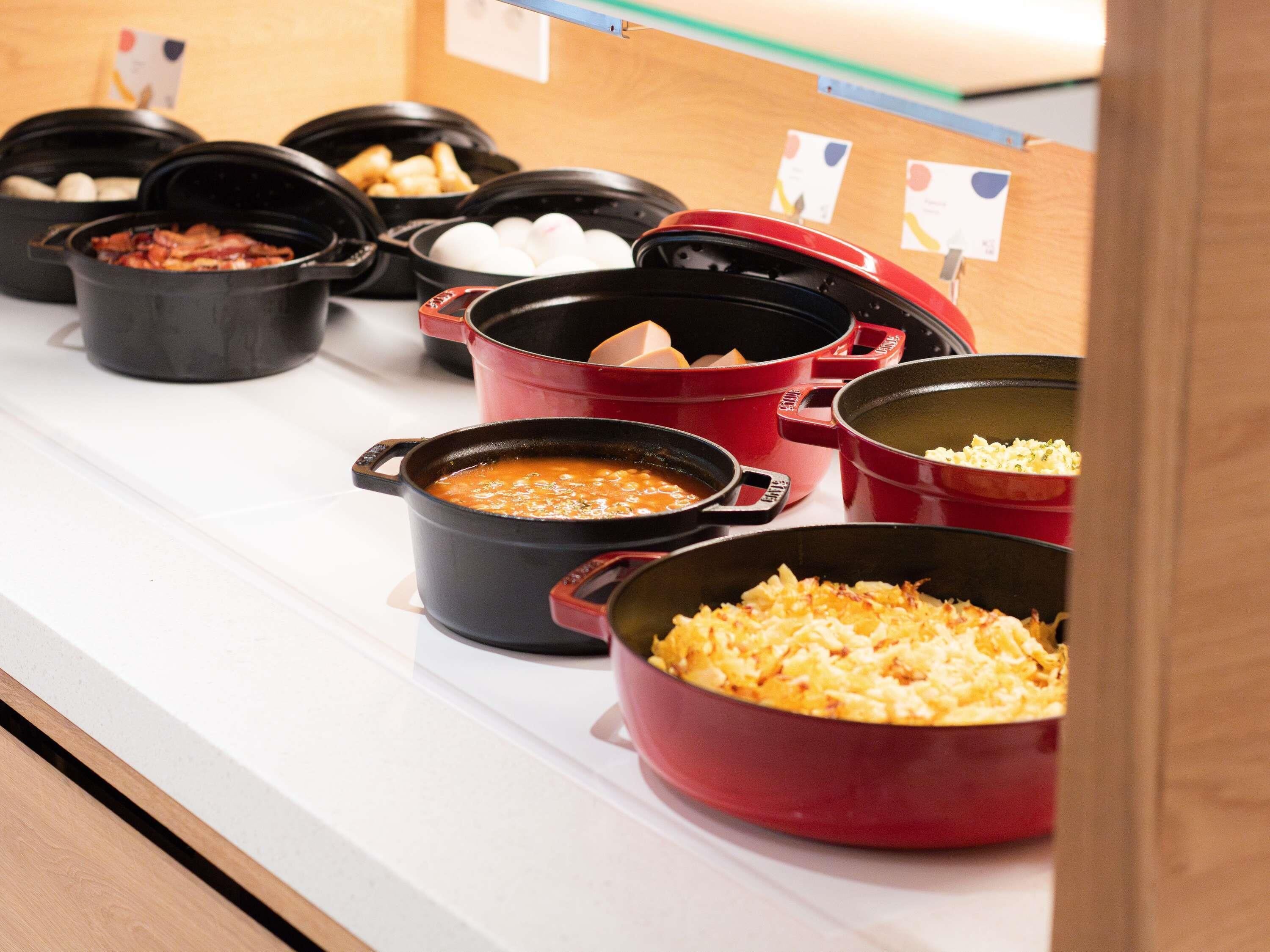 A buffet line with various dishes in black and red pots.