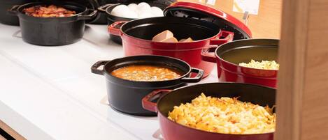 A buffet line with various dishes in black and red pots.