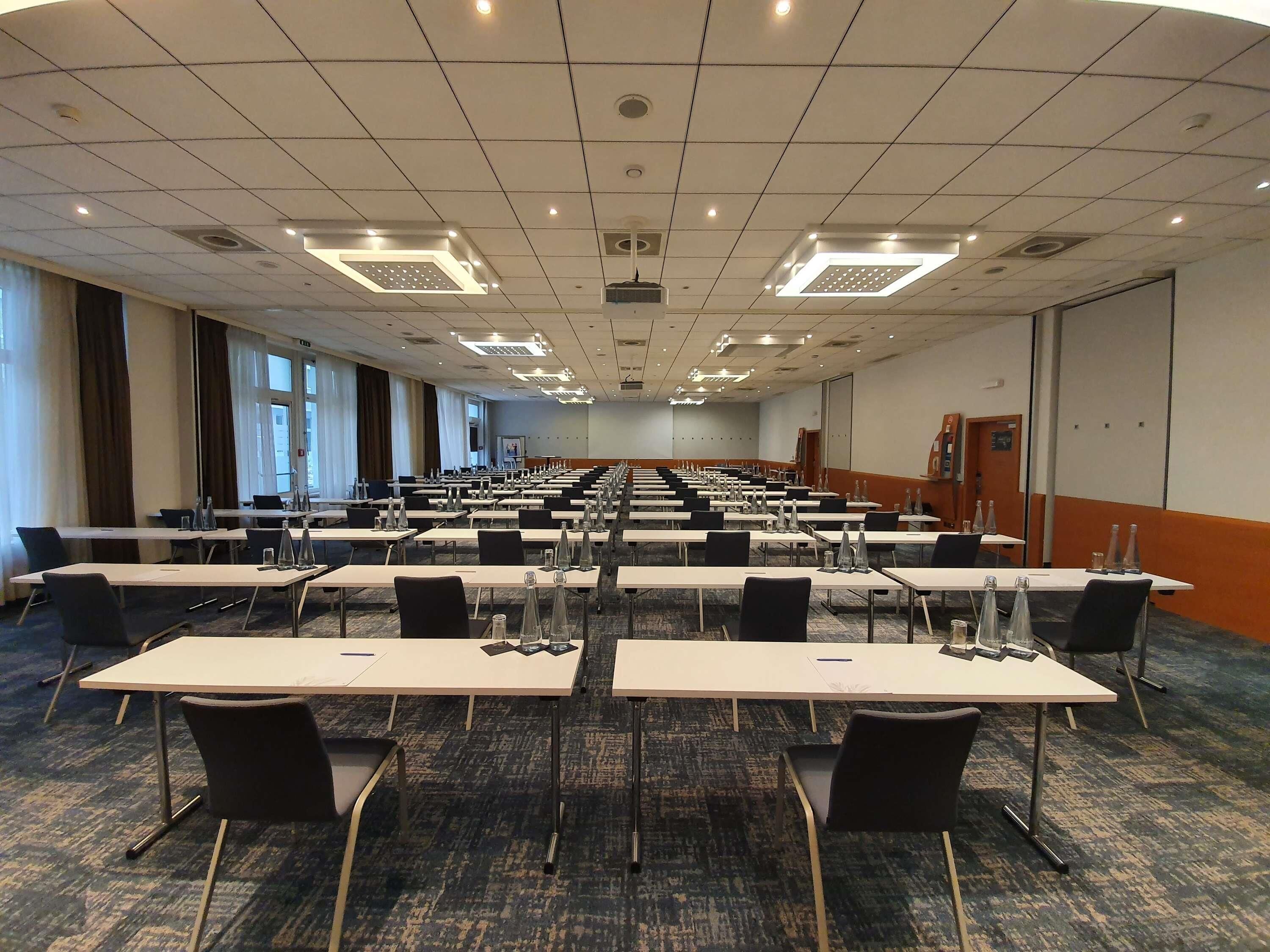 A conference room with rows of tables and chairs, equipped with water bottles and nameplates.