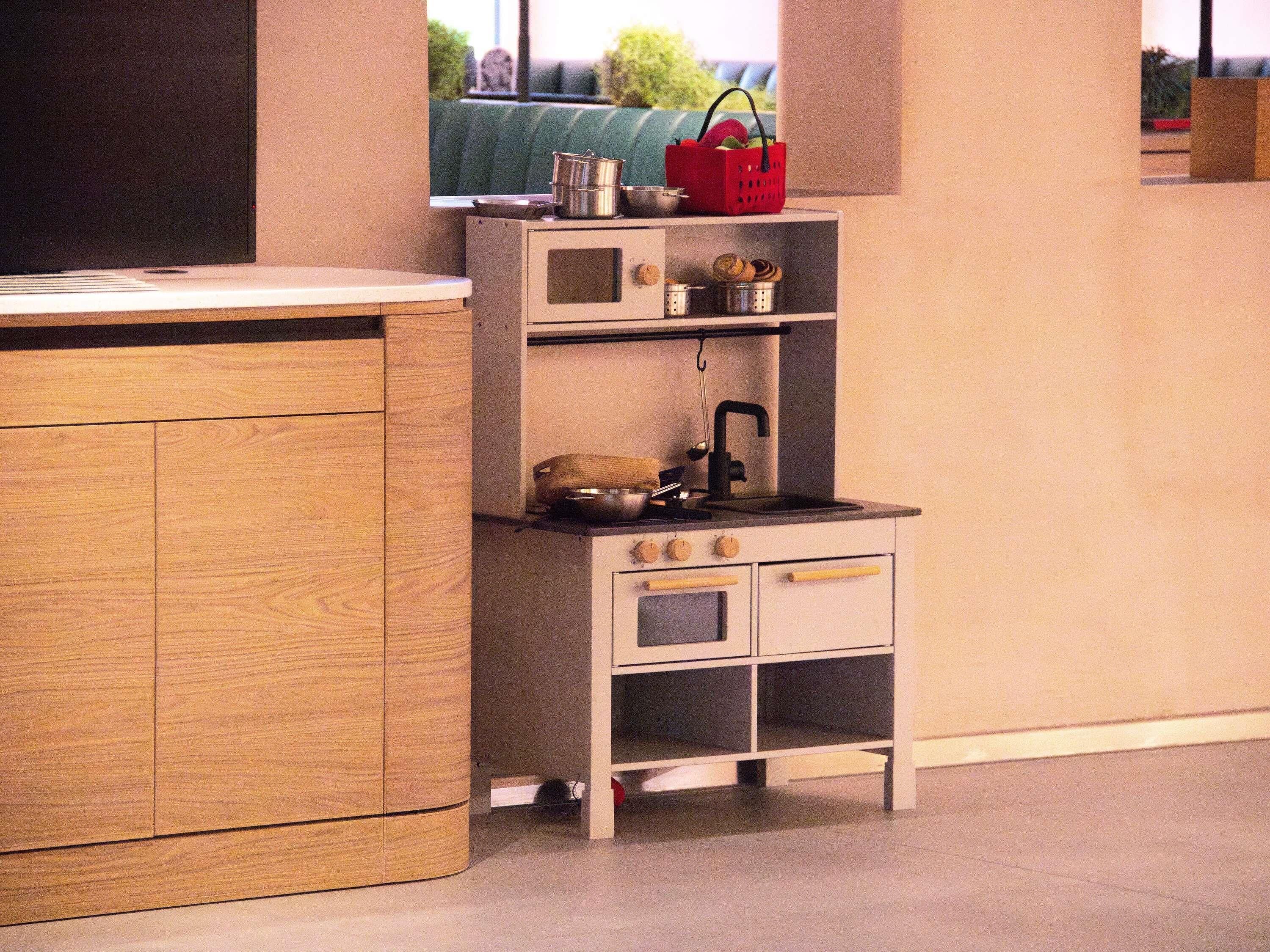 A compact kitchenette with a wooden cabinet, a small stove, and a shelf with kitchen utensils.