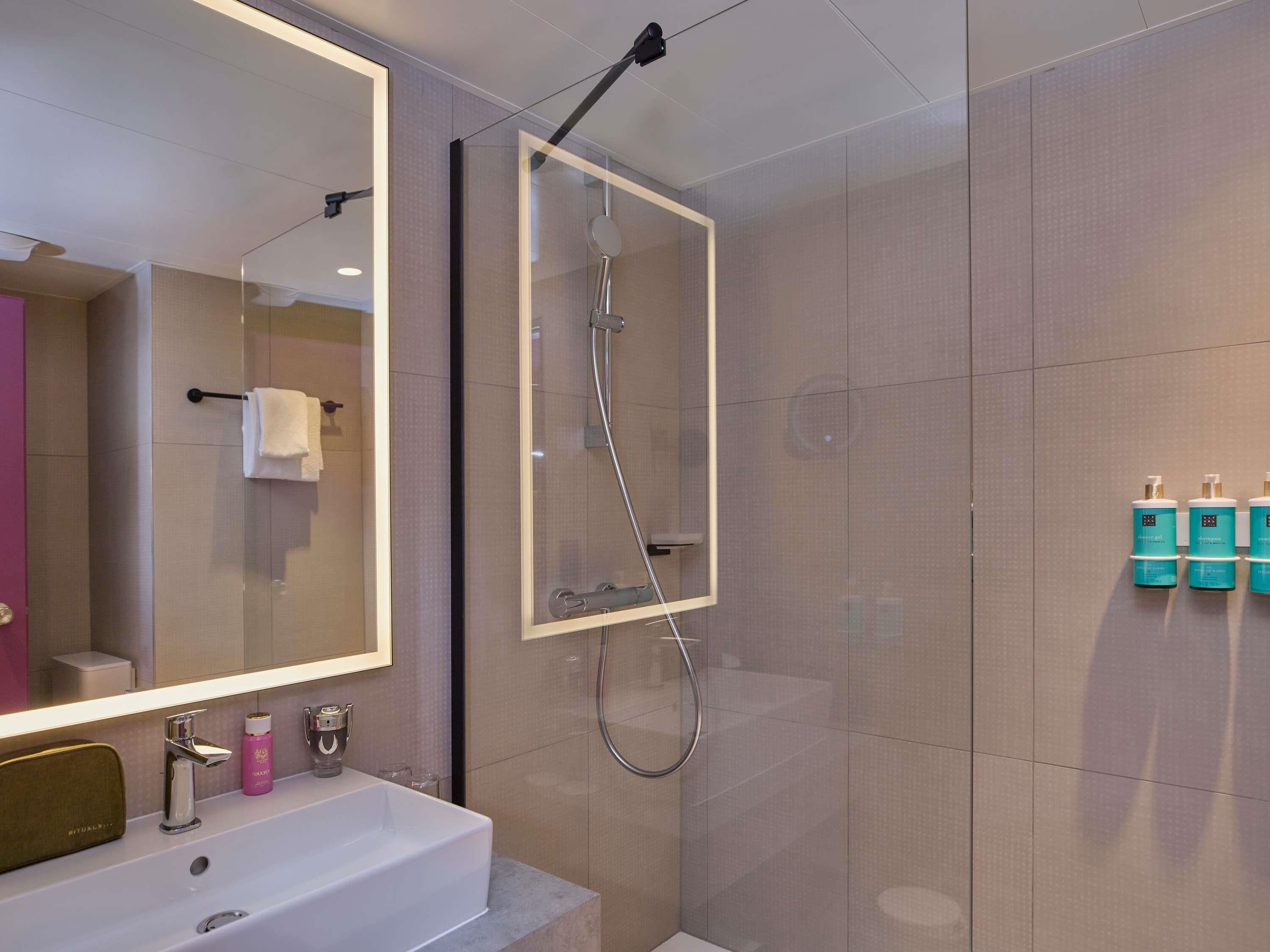 Un baño moderno con un espejo grande, ducha y lavabo.