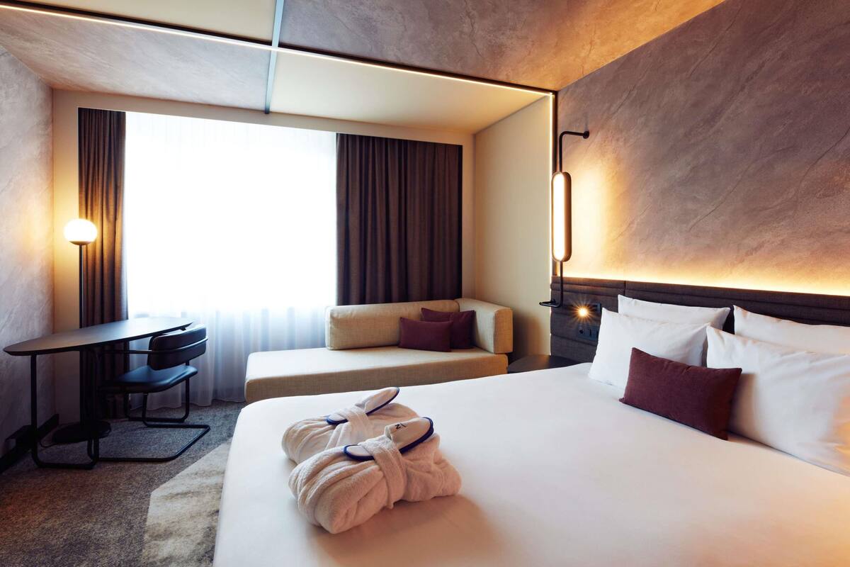 A hotel room with a large bed, a desk, a sofa, and a window with curtains.