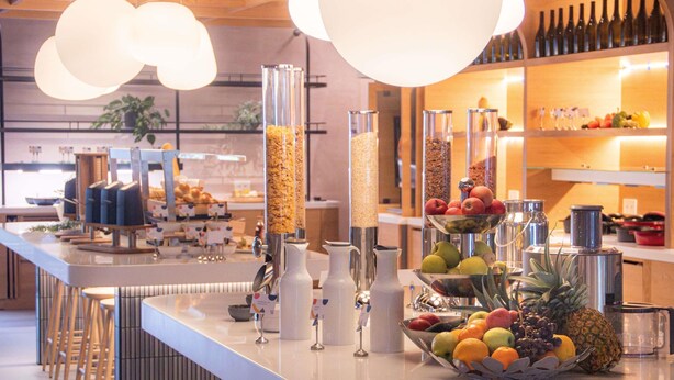 Una barra de desayuno moderna con diferentes dispensadores de alimentos, un frutero y taburetes.