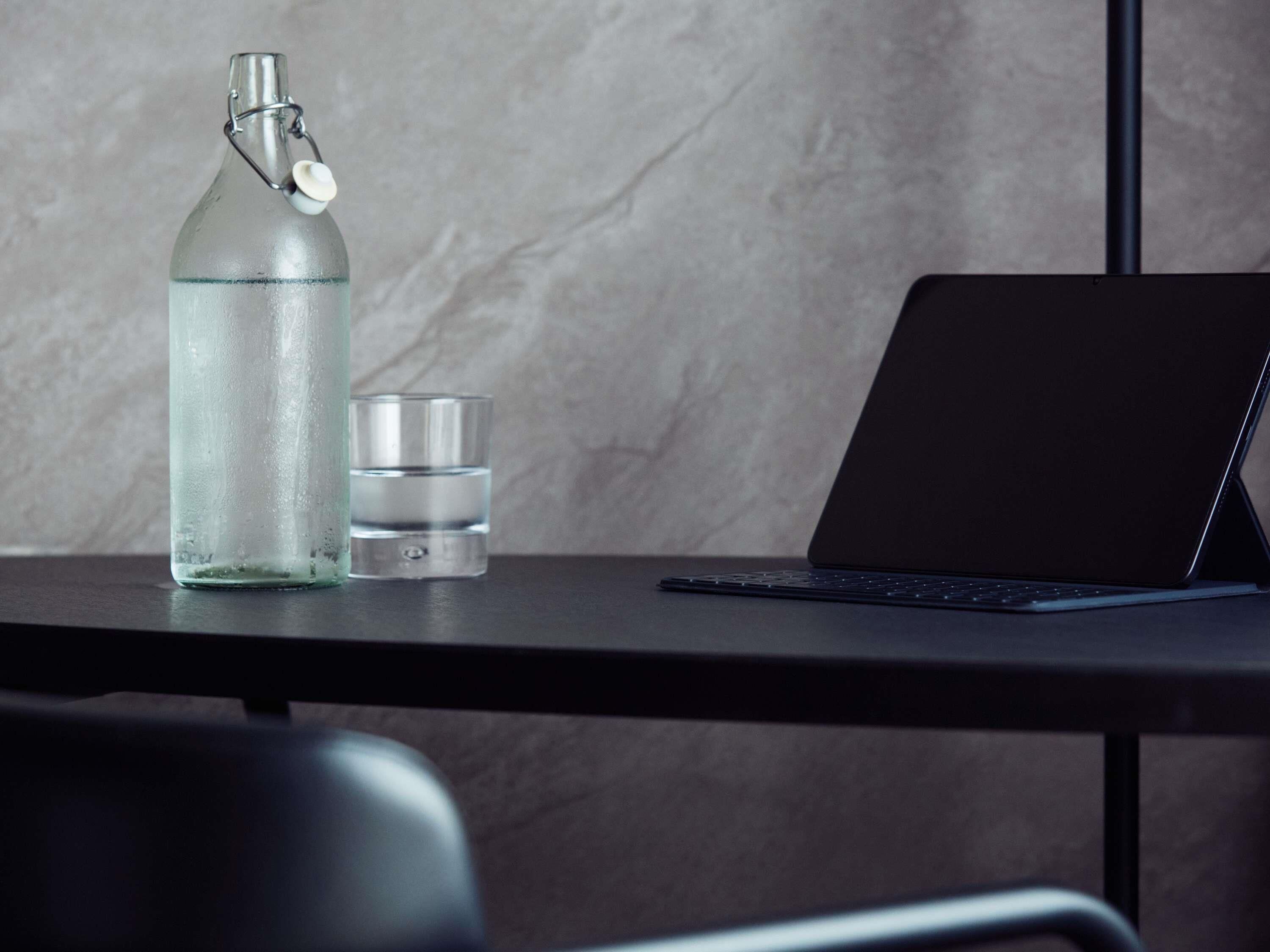 Ein Laptop auf einem Tisch, neben ihm eine schlichte Glasflasche und ein kleiner Behälter.