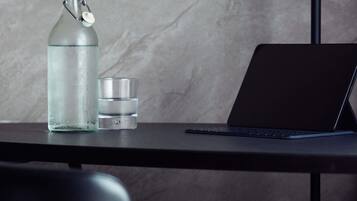 A laptop on a table with a clear glass bottle and a small container beside it.