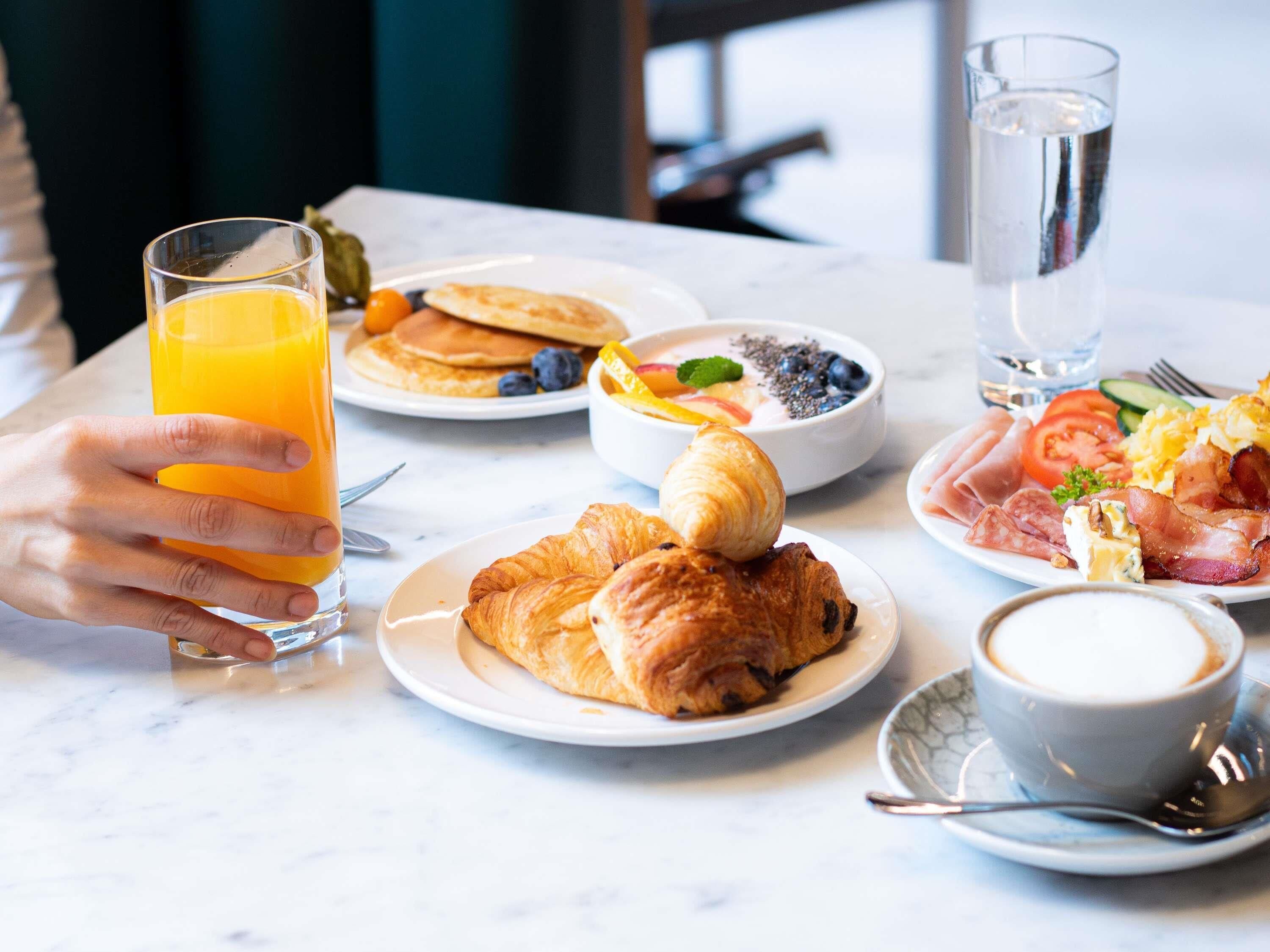 A breakfast setting with croissants, pancakes, eggs, bacon, and a glass of orange juice.