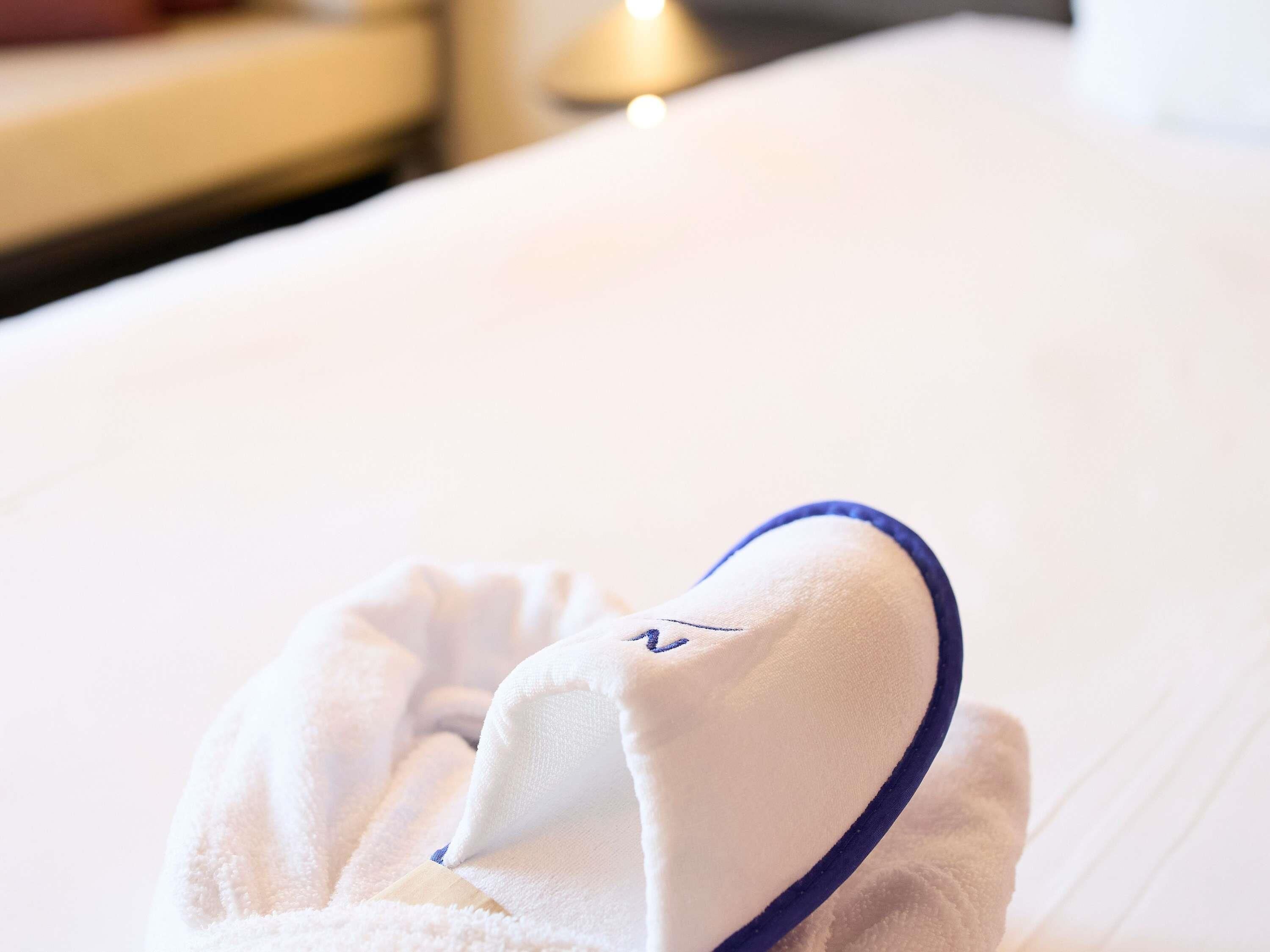 A neatly folded white towel with a blue trim on a bed.