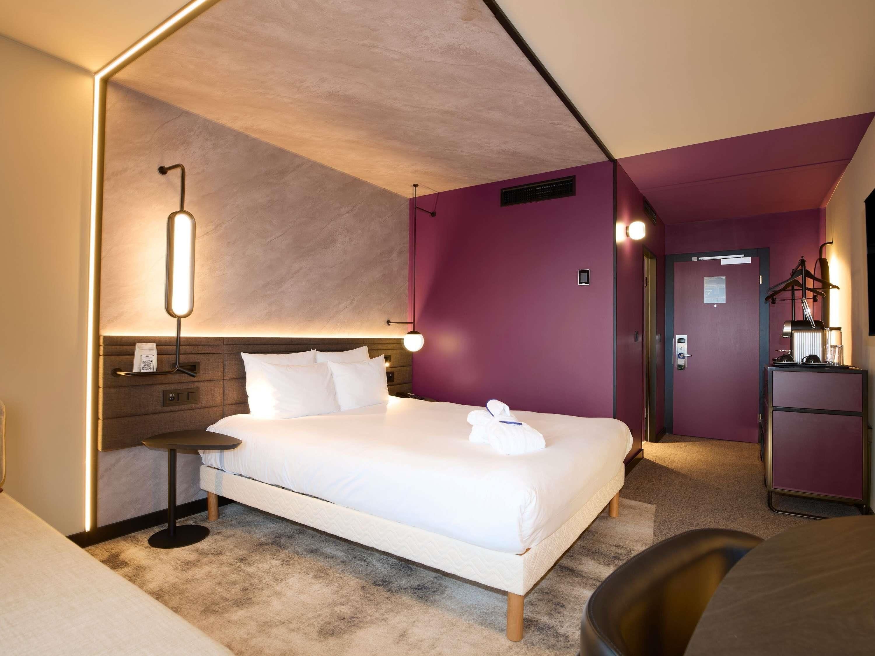 Quarto de hotel moderno com uma cama grande, mesas de cabeceira, uma escrivaninha e uma cadeira.