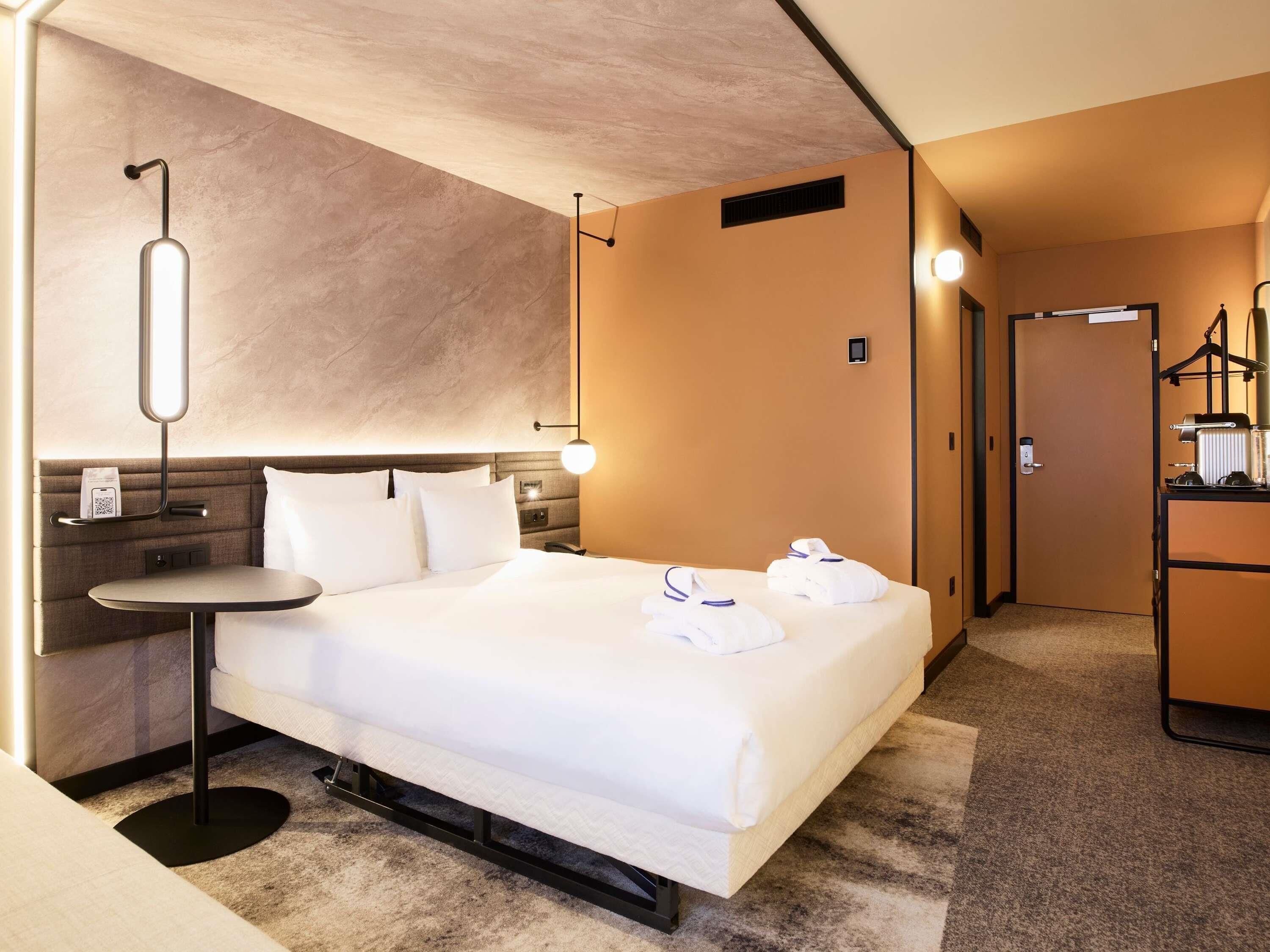 Une chambre d’hôtel avec un lit, une table de chevet et un petit bureau avec une lampe.