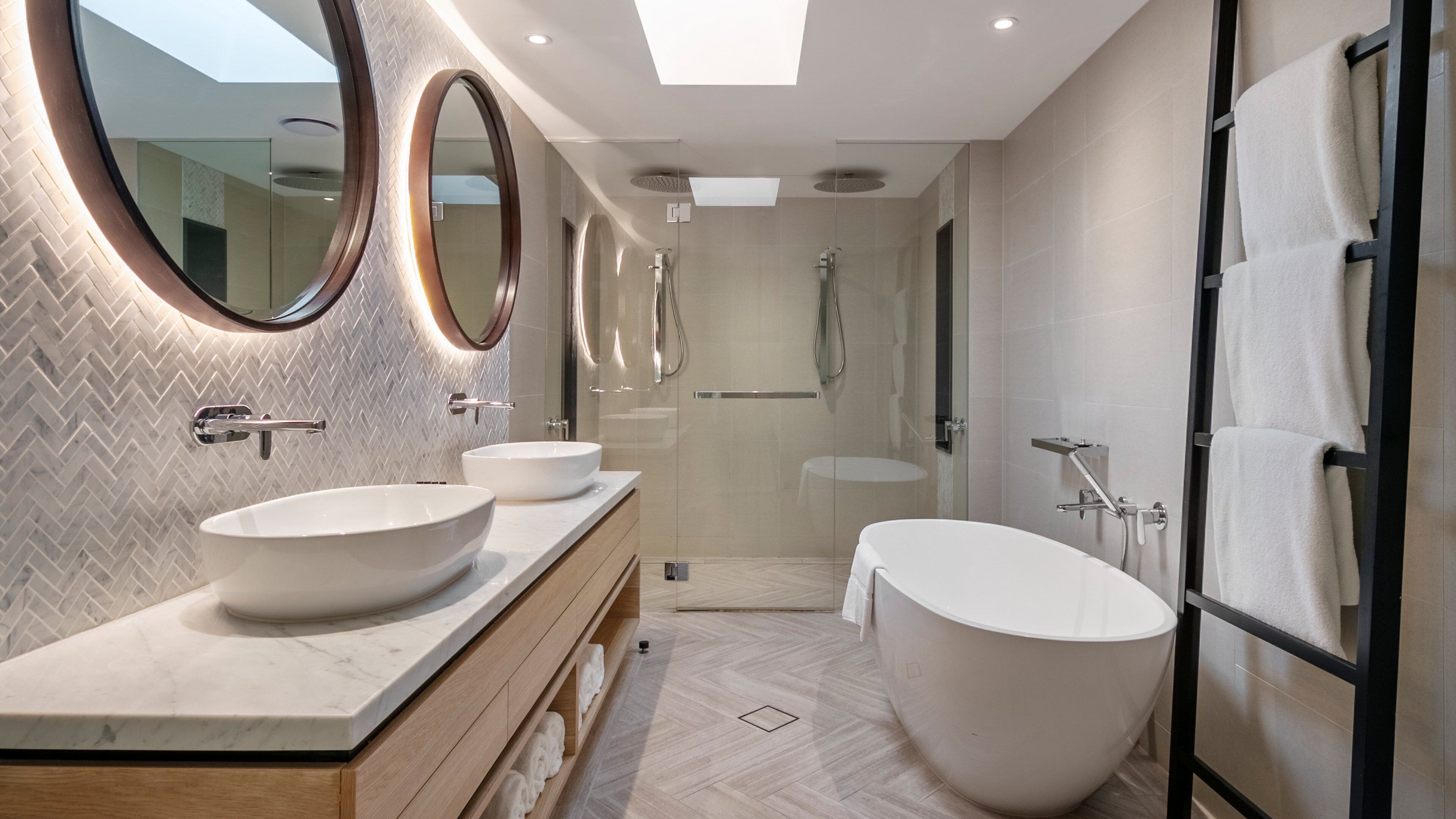 A modern bathroom with two sinks, a large bathtub, and a walk-in shower.