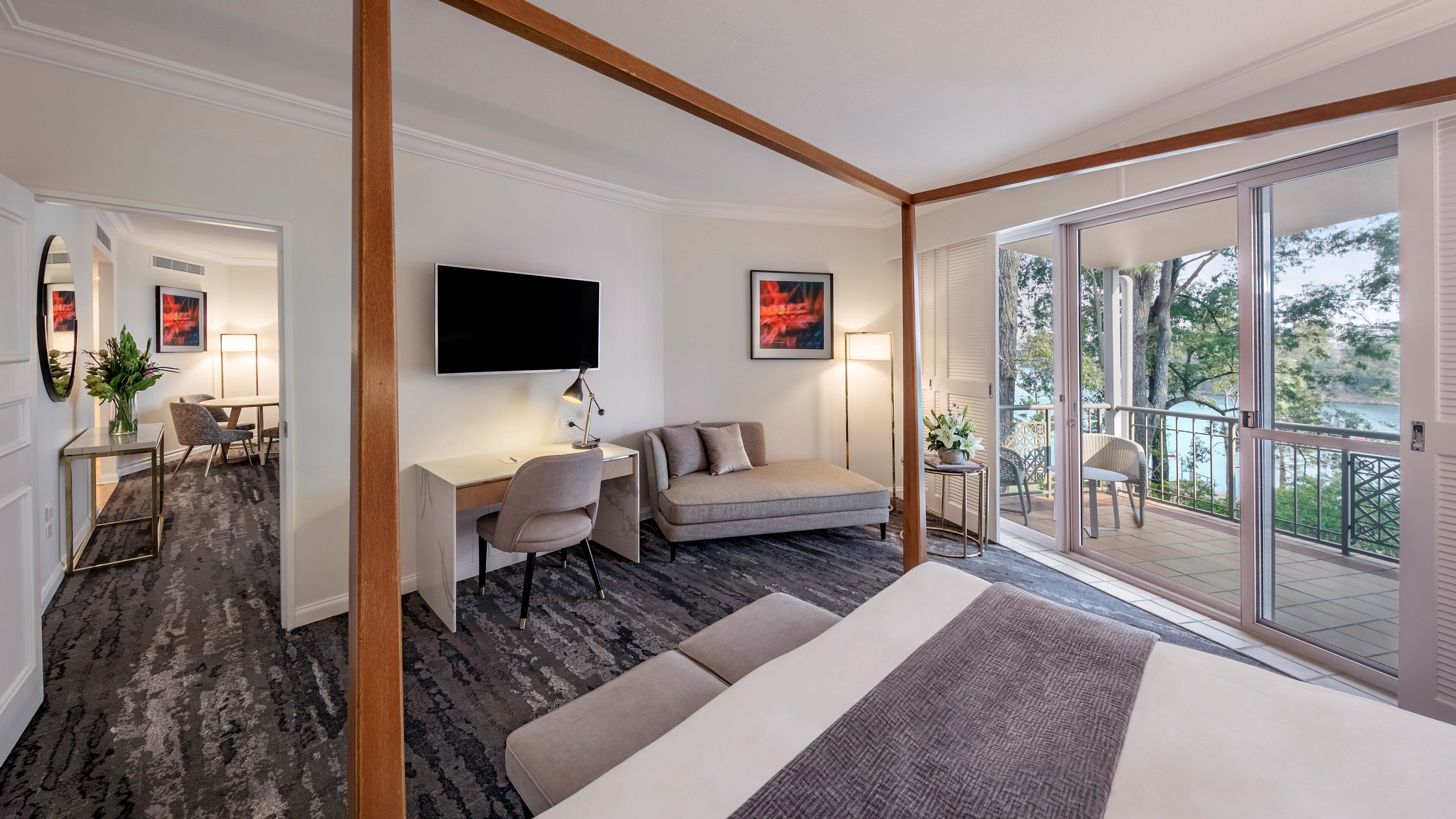 A modern hotel room with a large bed, a desk, a sofa, and a balcony with a view of the outdoors.