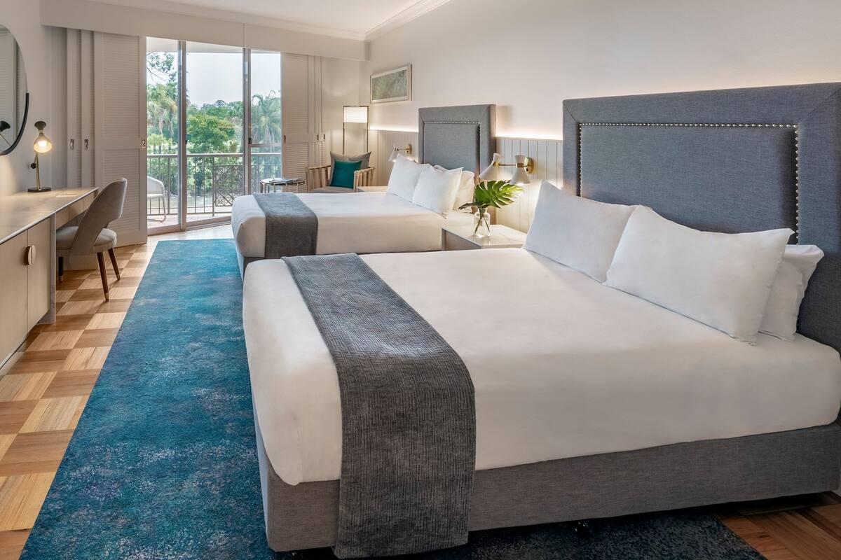 Une chambre d’hôtel avec deux lits, un bureau avec une télévision, une chaise, un balcon avec vue et une grande fenêtre.