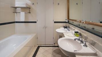 A modern bathroom with a bathtub, three sinks, and a large mirror.