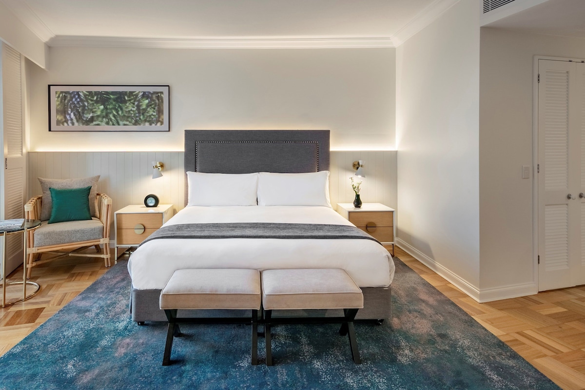 A modern bedroom with a large bed, bedside tables, a chair, and a view through a sliding door.