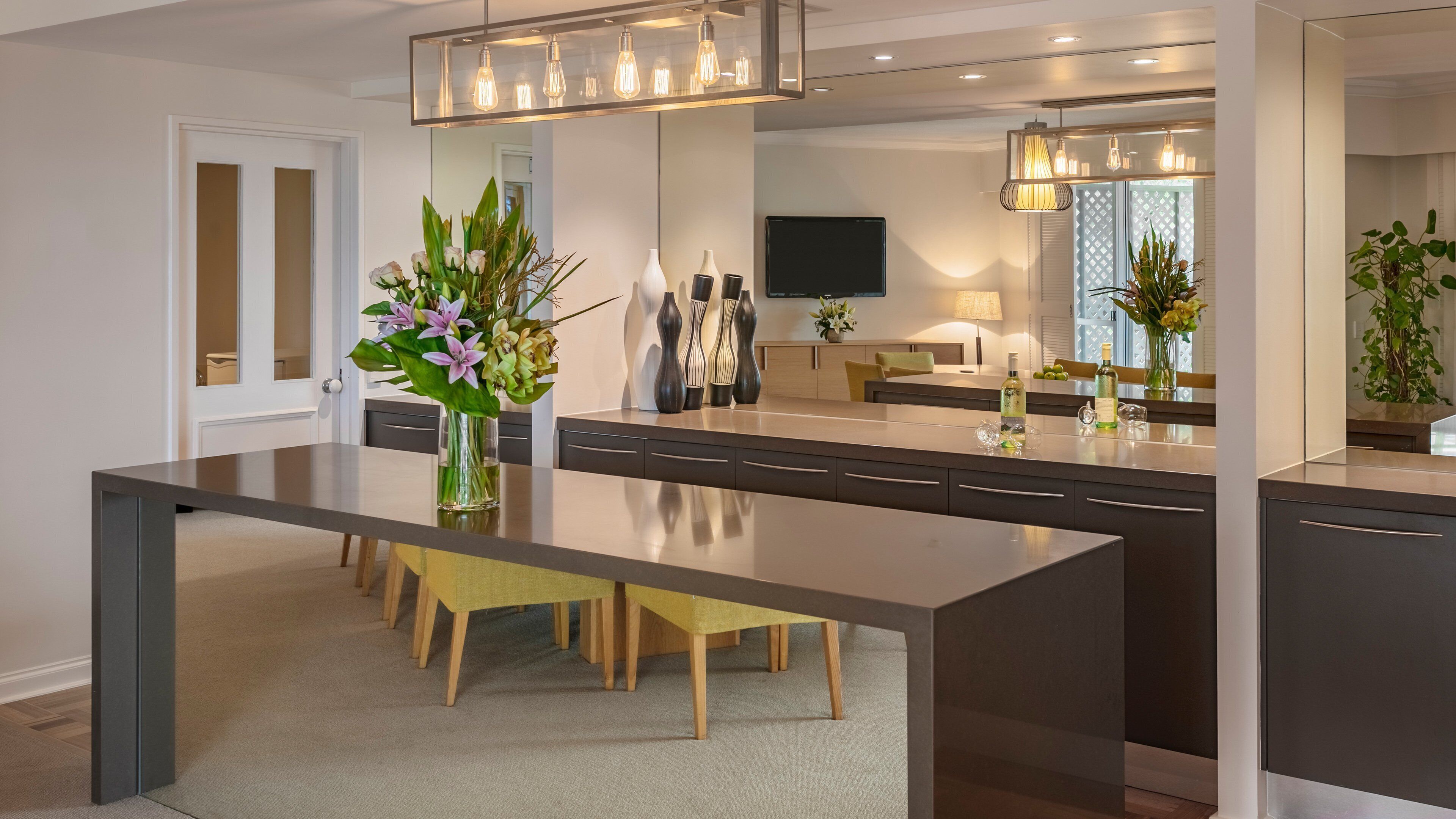 A modern kitchen with a central island, dark cabinetry, and a dining area with yellow chairs.