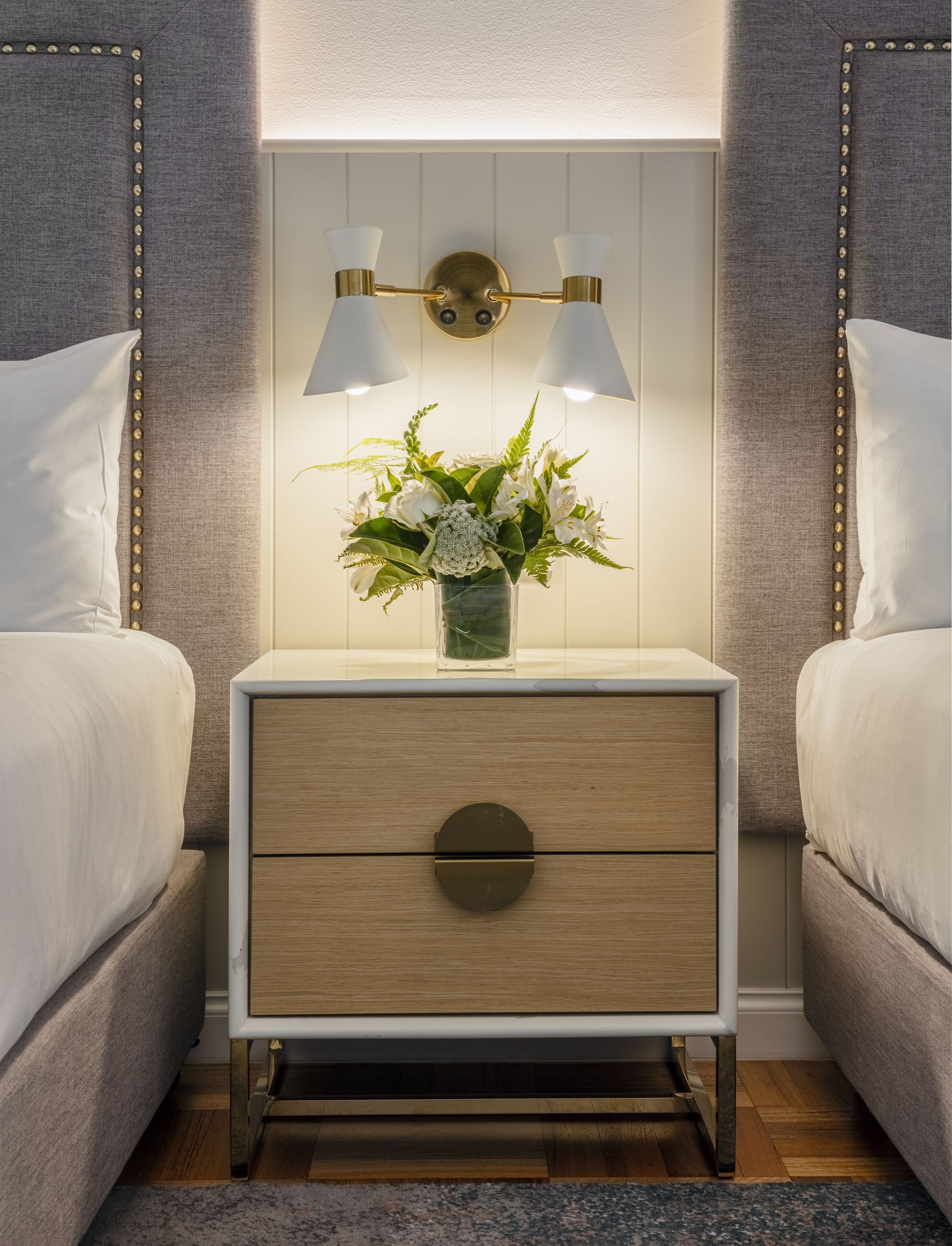 A bedroom with a nightstand, two bedside tables, a bed, and a wall-mounted light fixture.