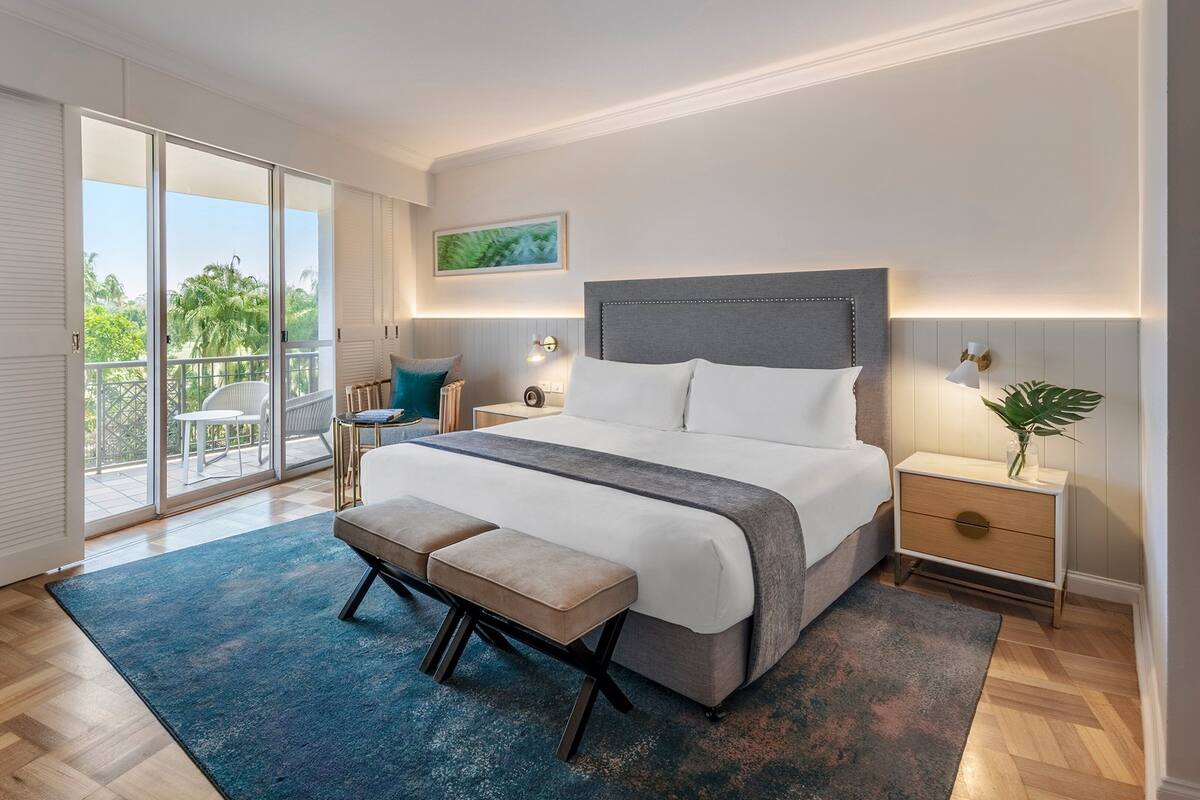 Une chambre à coucher moderne avec un grand lit, un banc, une table de chevet et une vue sur l’extérieur.