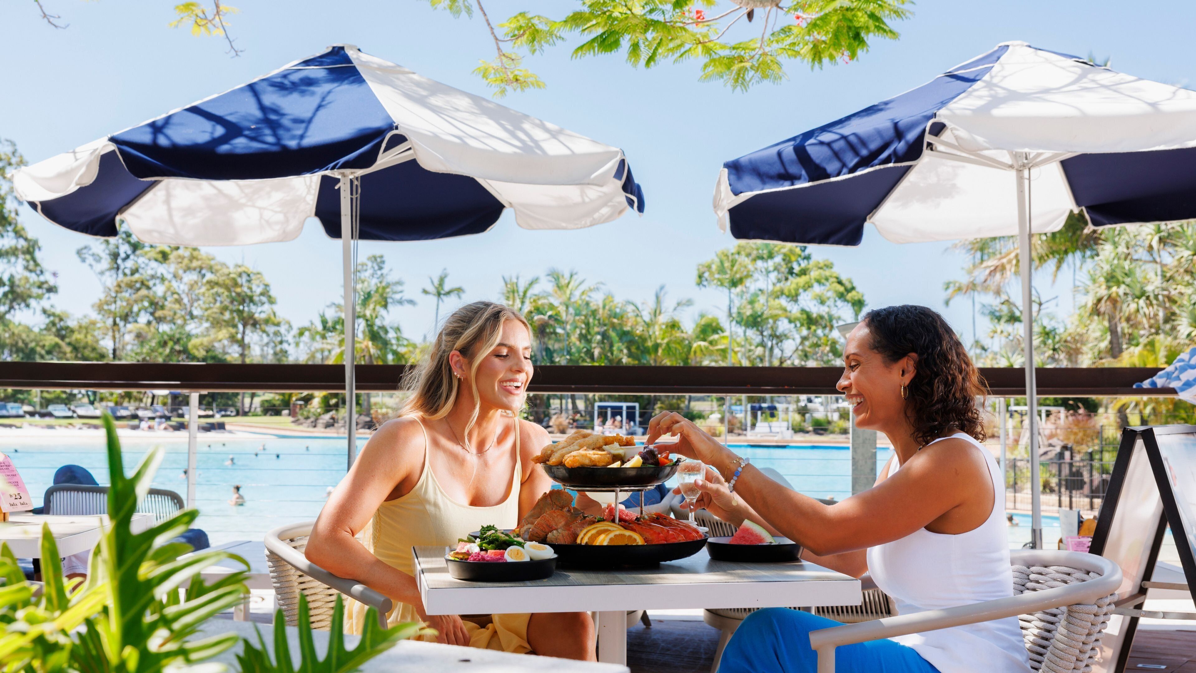 Two people dining at an outdoor table with a view of a pool and palm trees.