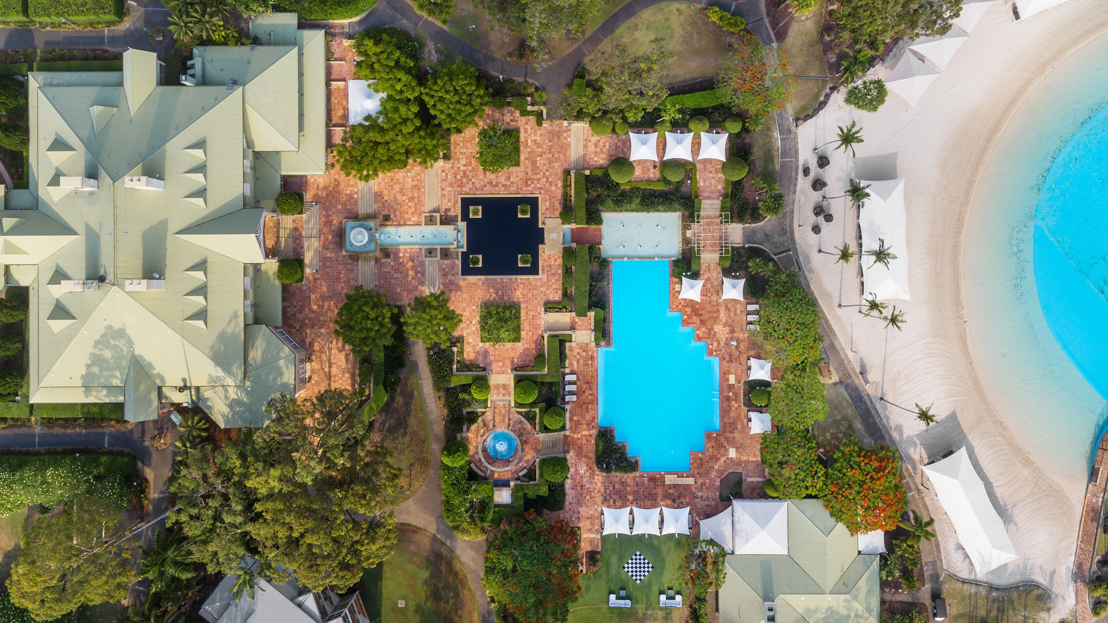 Vue aérienne d’un complexe hôtelier doté d’une piscine, d’espaces de détente et d’une plage.