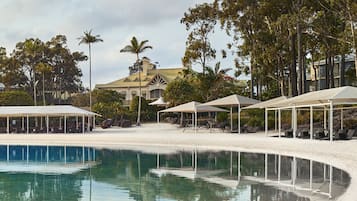 A resort with a pool, beach umbrellas, lounge chairs, and a large building with a green roof.