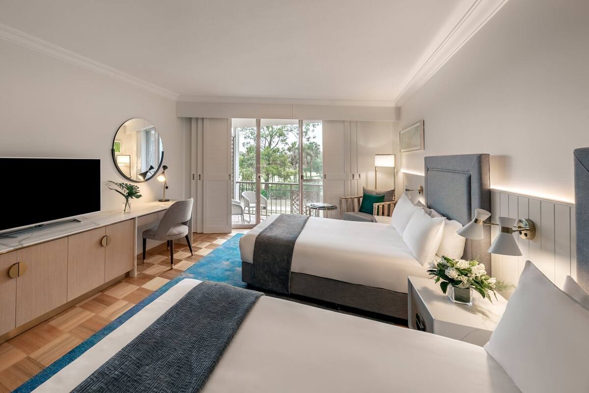 Une chambre d’hôtel avec un lit, un bureau, une télévision, une chaise et un balcon donnant sur la verdure.