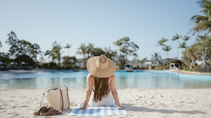A person sitting on a beach towel by a pool with a straw hat, a bag, and sandals. - InterContinental Sanctuary Cove Resort by IHG (Hope Island)