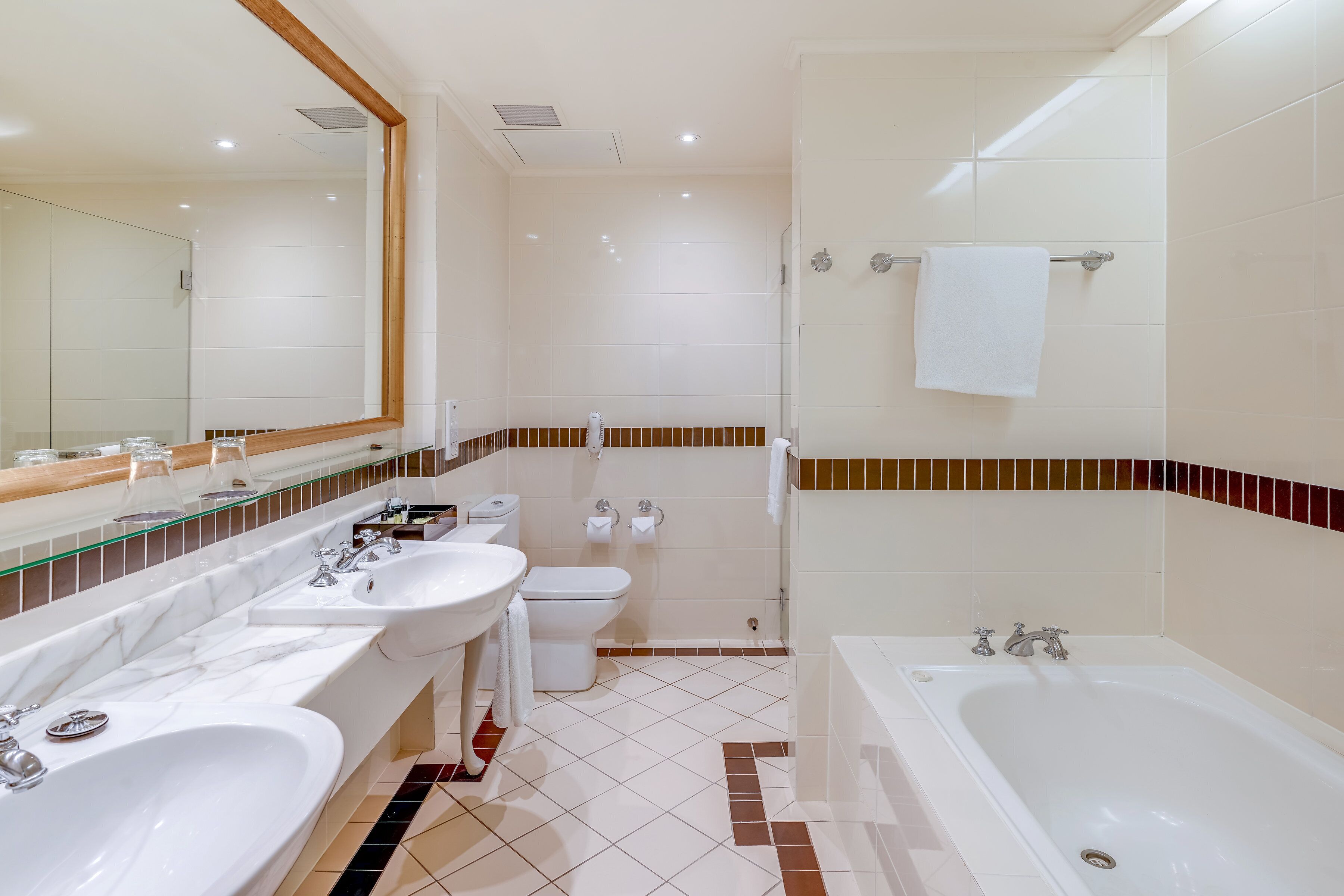 A modern bathroom with a large mirror, two sinks, a toilet, and a bathtub.