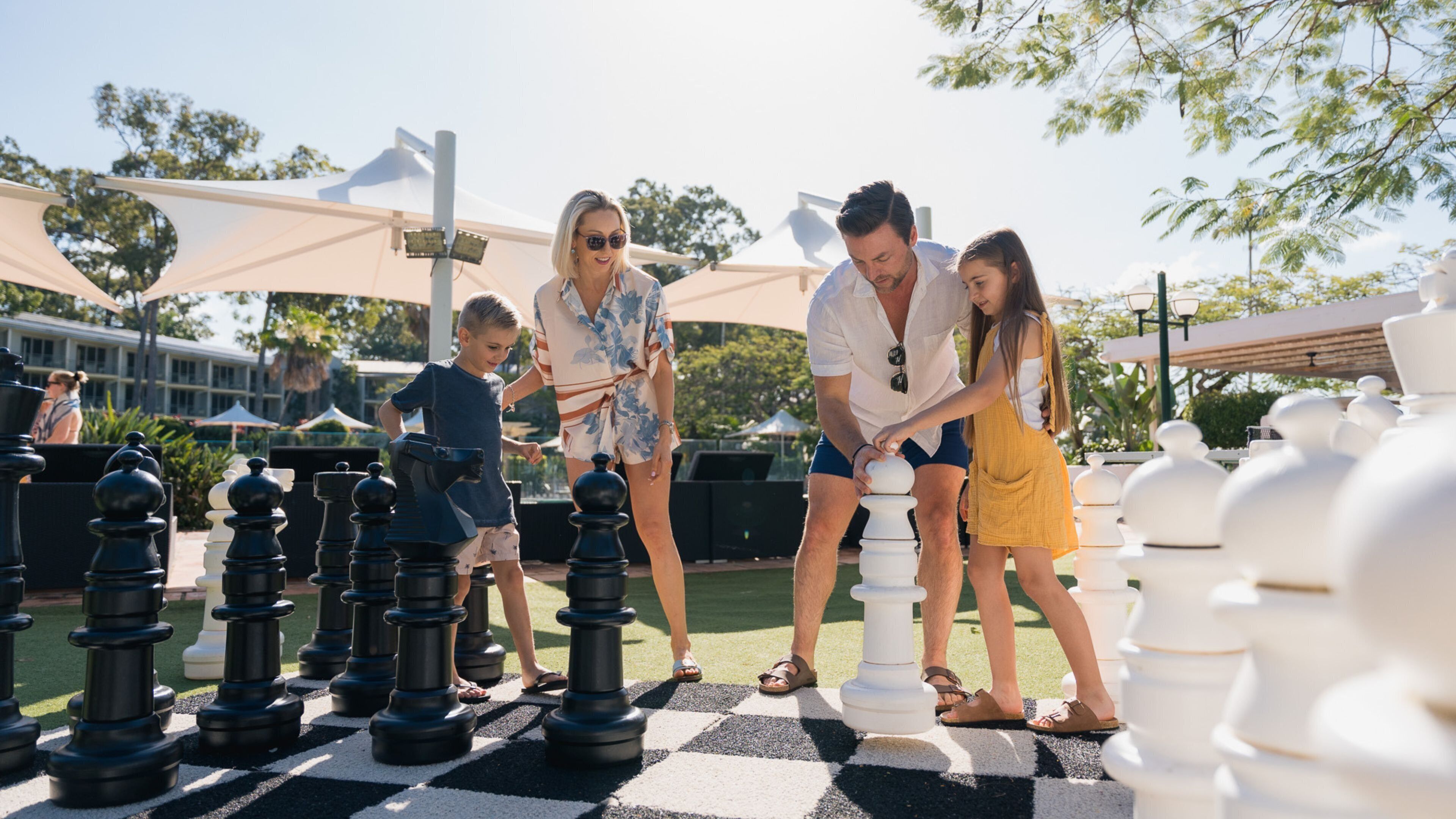 A group of people playing a large outdoor chess game on a checkered ground.